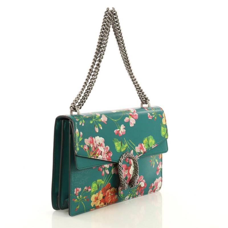This Gucci Dionysus Bag Blooms Print Leather Medium, crafted from green blooms print leather, features sliding chain strap, tiger head spur detail on flap, and aged silver-tone hardware. Its pin closure with side release opens to a neutral fabric