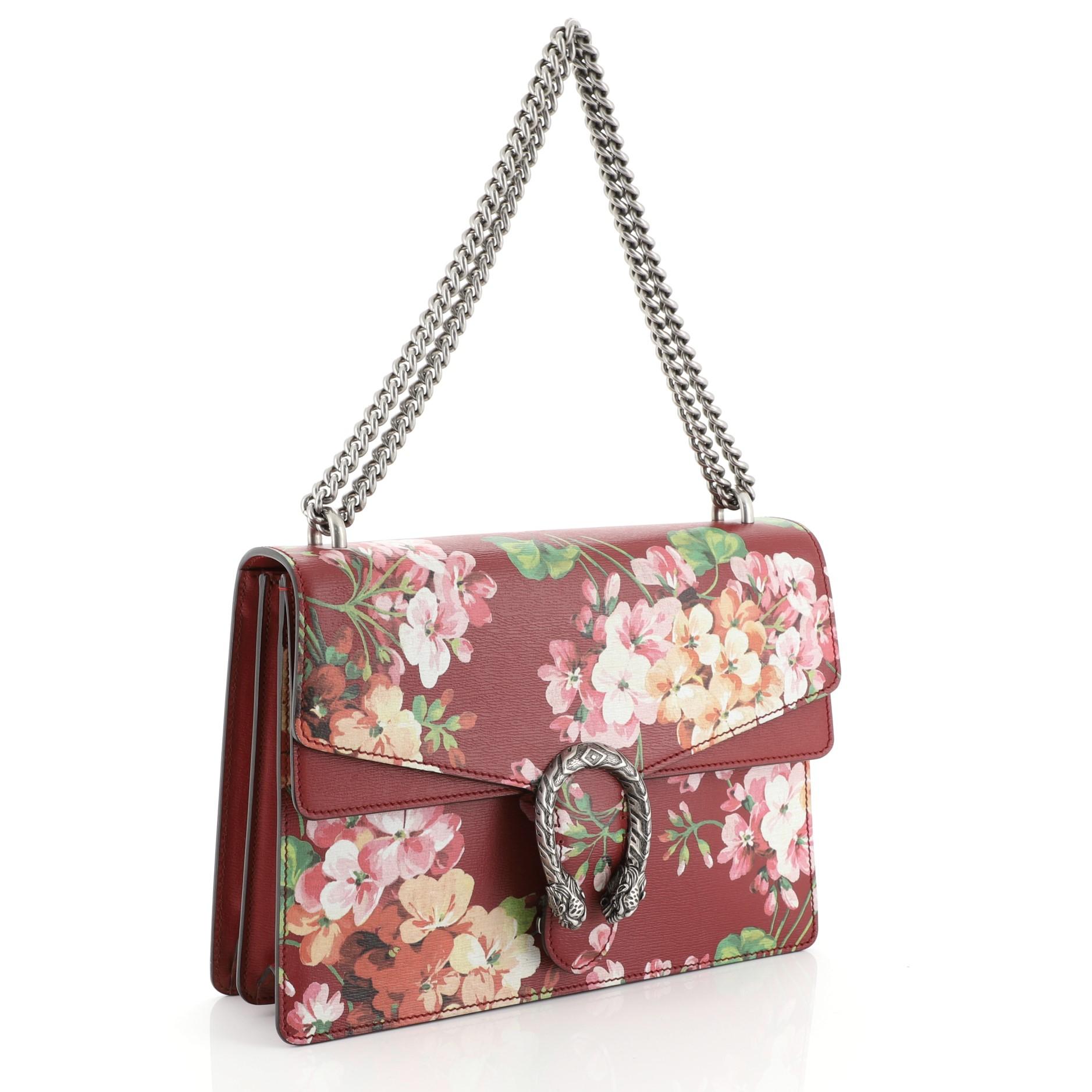 This Gucci Dionysus Bag Blooms Print Leather Medium, crafted from red blooms print leather, features sliding chain strap, tiger head spur detail on flap, and aged silver-tone hardware. Its pin closure with side release opens to a neutral fabric