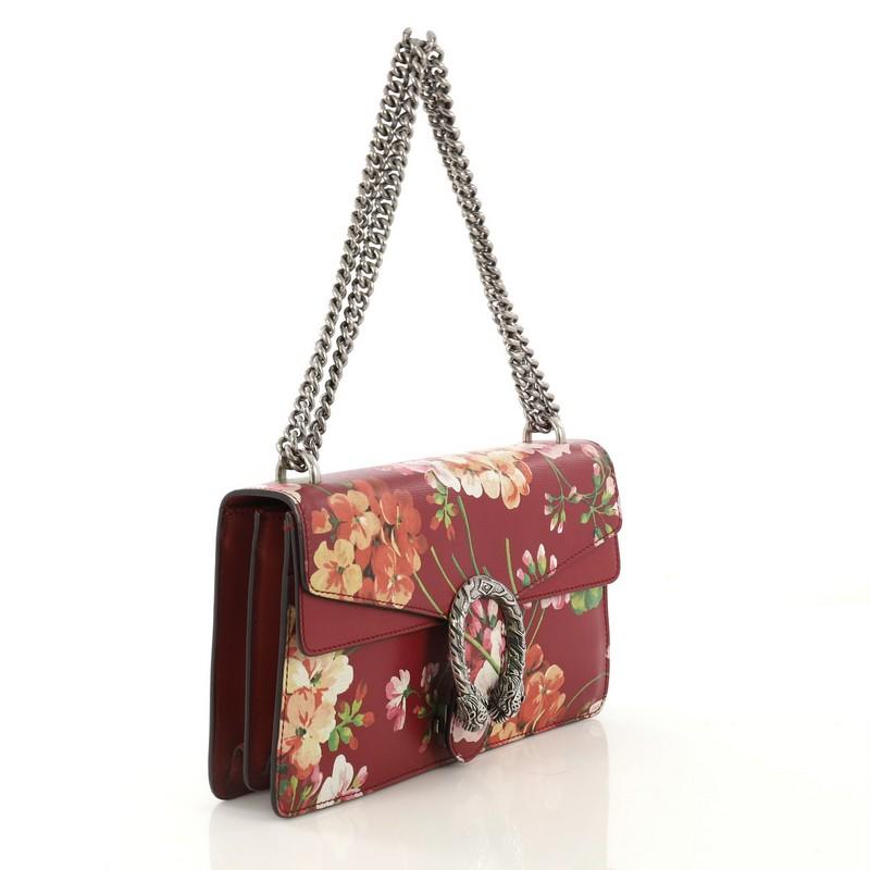 This Gucci Dionysus Bag Blooms Print Leather Small, crafted from red leather with floral print, features a sliding chain strap, tiger head spur detail on flap, and aged silver-tone hardware. Its pin closure with side release opens to a neutral