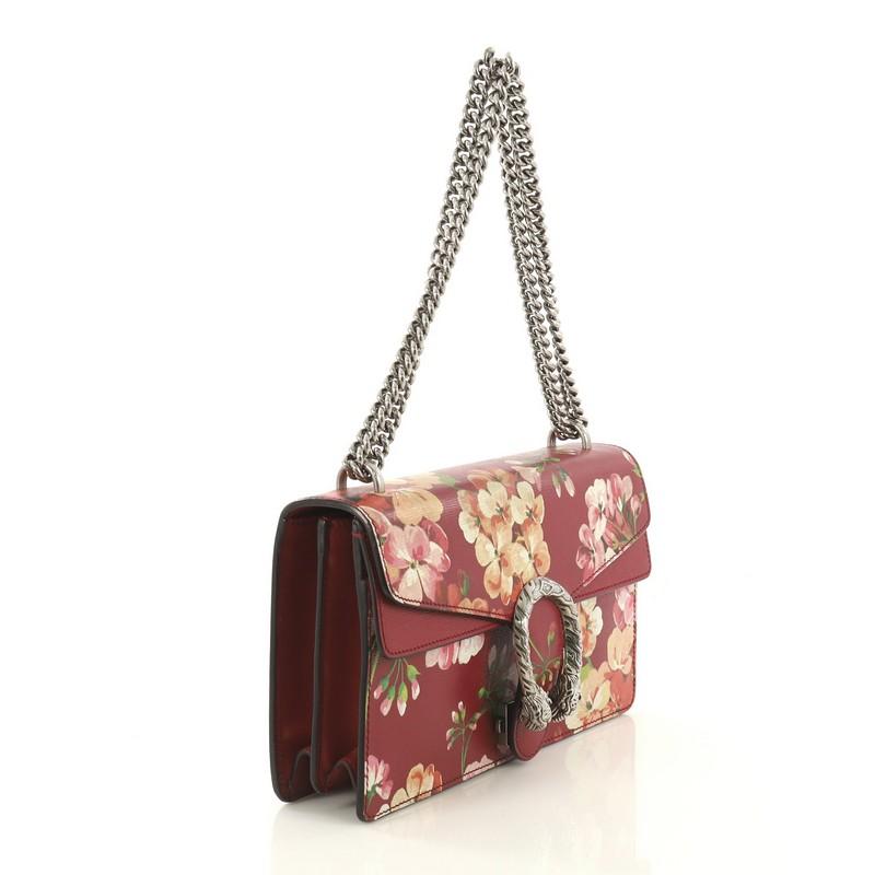 This Gucci Dionysus Bag Blooms Print Leather Small, crafted from red leather with floral print, features sliding chain strap, tiger head spur detail on flap, and aged silver-tone hardware. Its pin closure with side release opens to a neutral fabric