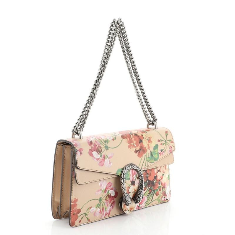 This Gucci Dionysus Bag Blooms Print Leather Small, crafted from neutral leather with floral print, features sliding chain strap, tiger head spur detail on flap, and matte silver-tone hardware. Its pin closure with side release opens to a neutral