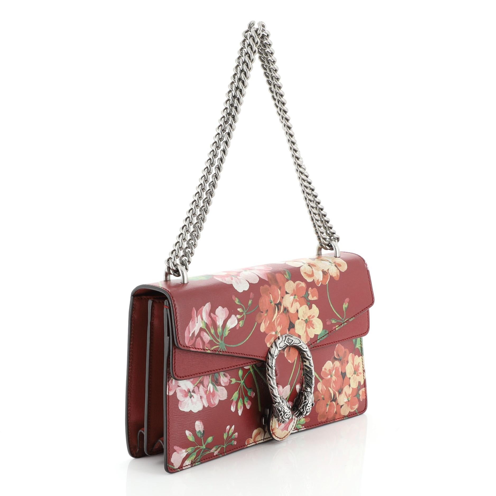 This Gucci Dionysus Bag Blooms Print Leather Small, crafted from red leather with blooms print, features sliding chain strap, tiger head spur detail on flap, and aged silver-tone hardware. Its pin closure with side release opens to a neutral fabric