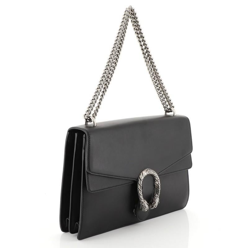 This Gucci Dionysus Bag Leather Medium, crafted from black leather, features a chain link strap, textured tiger head spur detail on its flap, and aged silver-tone hardware. Its hidden push-pin closure opens to a neutral and black printed fabric