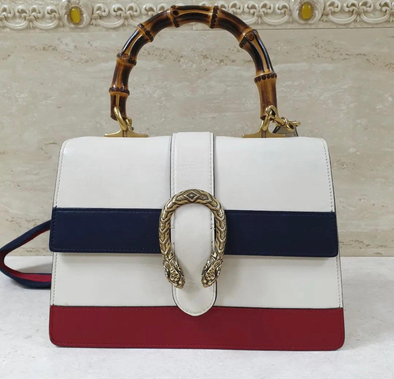 
Description

Crafted in a fine grained leather in white with contrast blue and red stripes. Designed with signature Dionysus textured tiger head buckle closure and a bamboo top handle. Features a detachable and adjustable web striped canvas