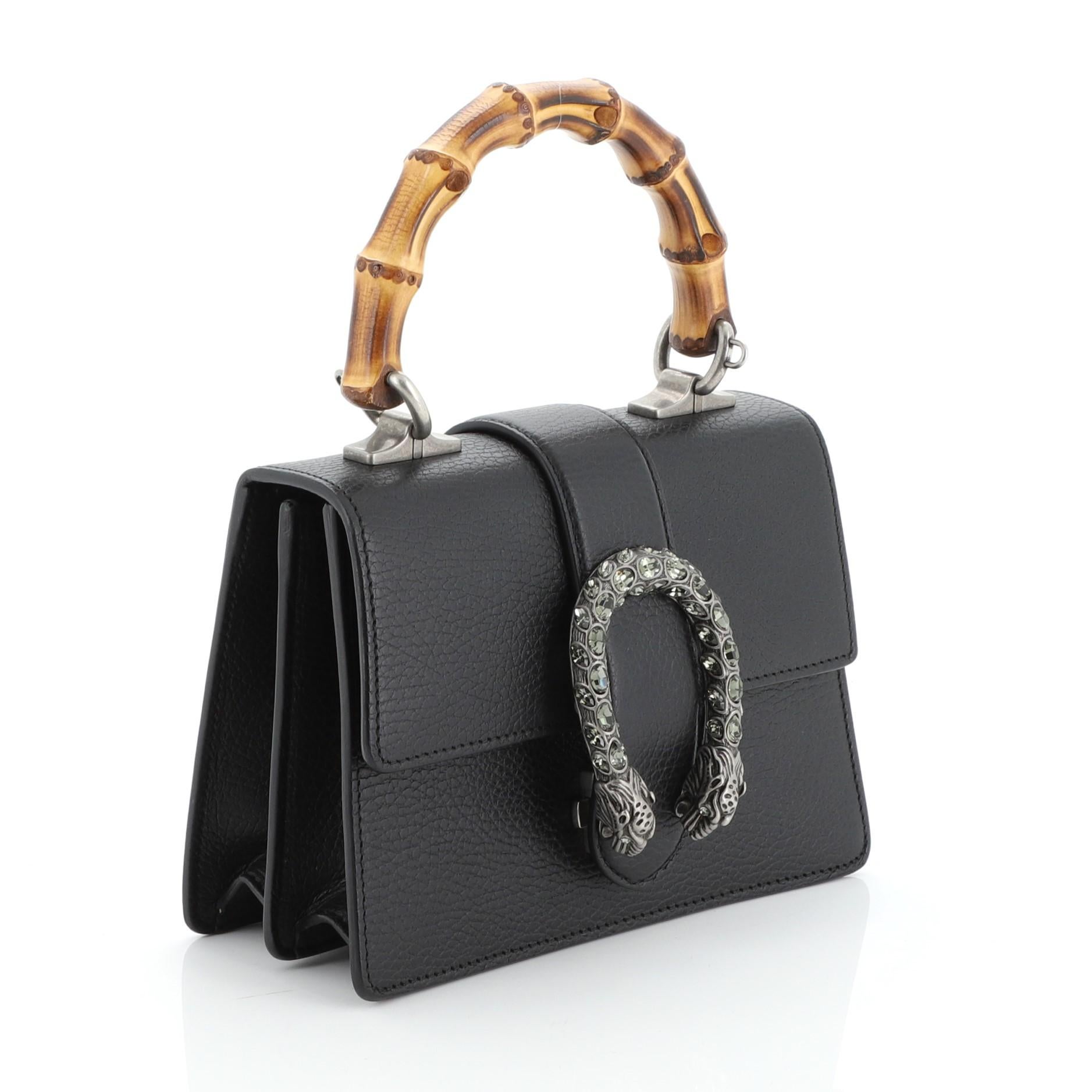 This Gucci Dionysus Bamboo Top Handle Bag Leather Mini, crafted from black leather, features a bamboo top handle, textured tiger head spur detail on its flap, and aged silver-tone hardware. Its flap closure with side release opens to a neutral