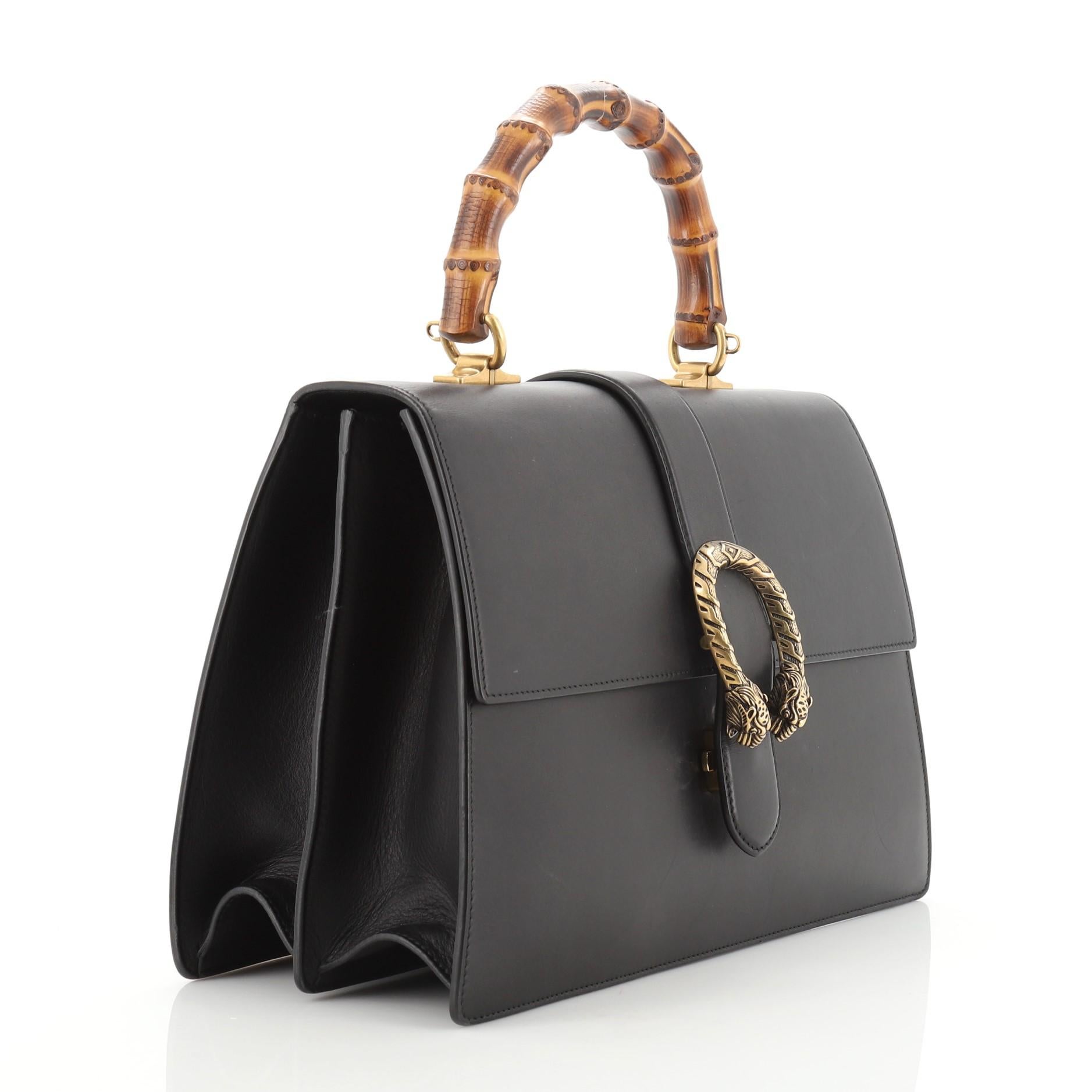This Gucci Dionysus Bamboo Top Handle Bag Leather Large, crafted from black leather, features a bamboo top handle, textured tiger head spur detail on its flap, and aged gold-tone hardware. Its flap closure with side release opens to a neutral fabric