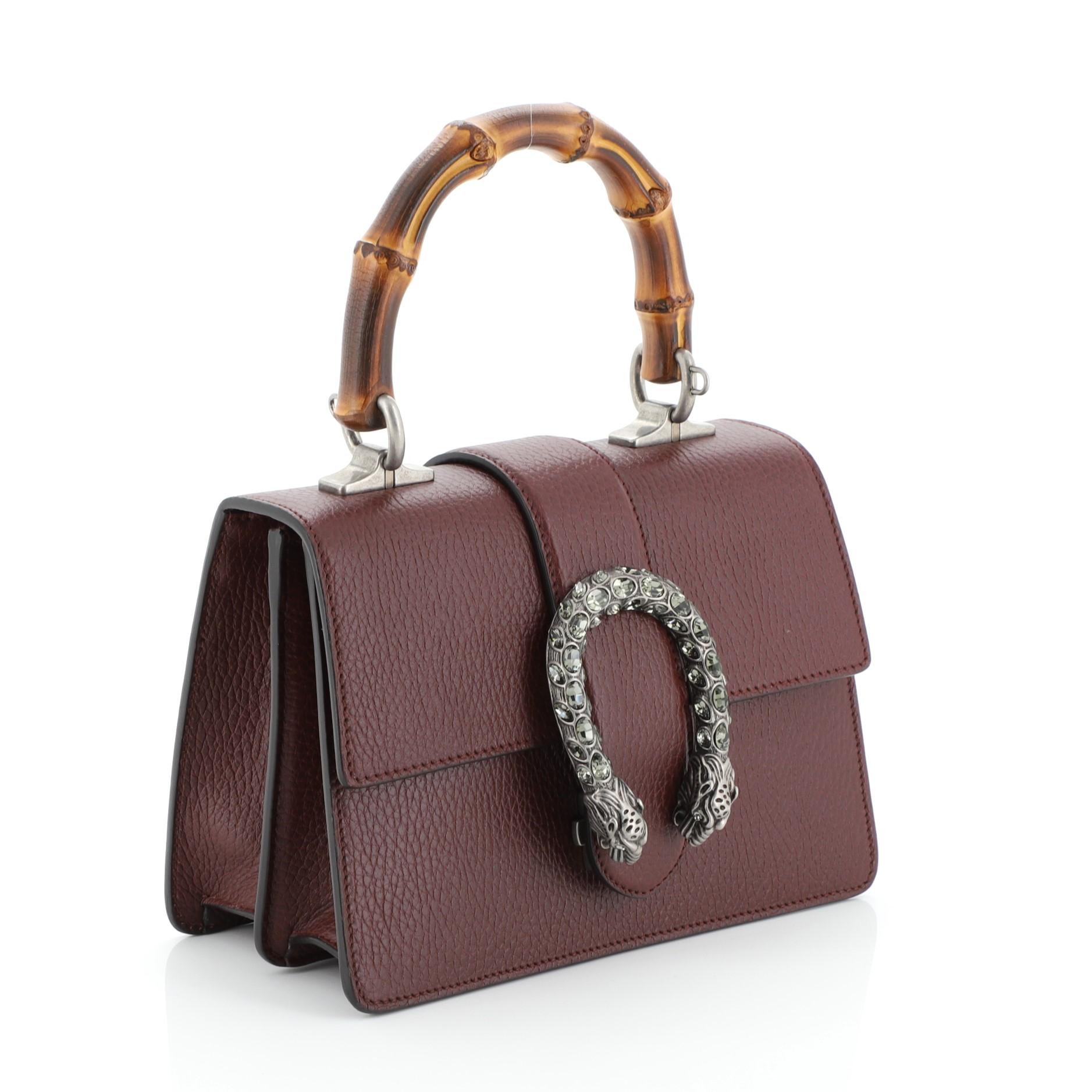 This Gucci Dionysus Bamboo Top Handle Bag Leather Mini, crafted from red leather, features a bamboo top handle, textured tiger head spur detail on its flap, and aged silver-tone hardware. Its flap closure with side release opens to a neutral fabric