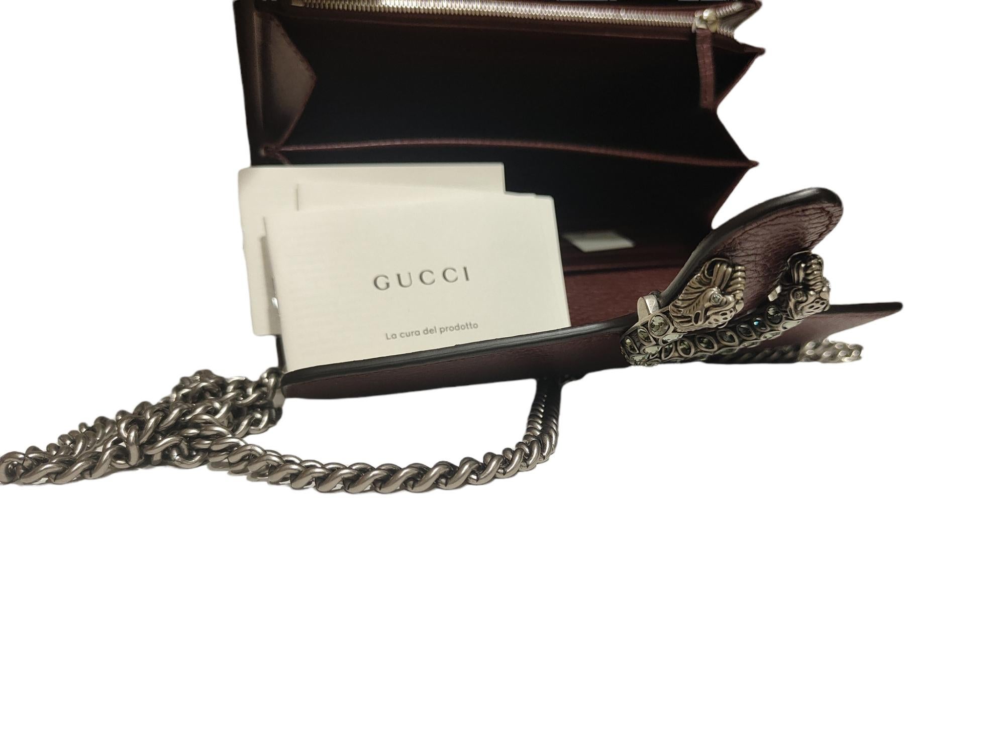A structured leather chain mini bag or wallet with textured tiger head spur closure-a unique detail referencing the Greek god Dionysus, who in myth is said to have crossed the river Tigris on a tiger sent to him by Zeus. The tiger head closure is