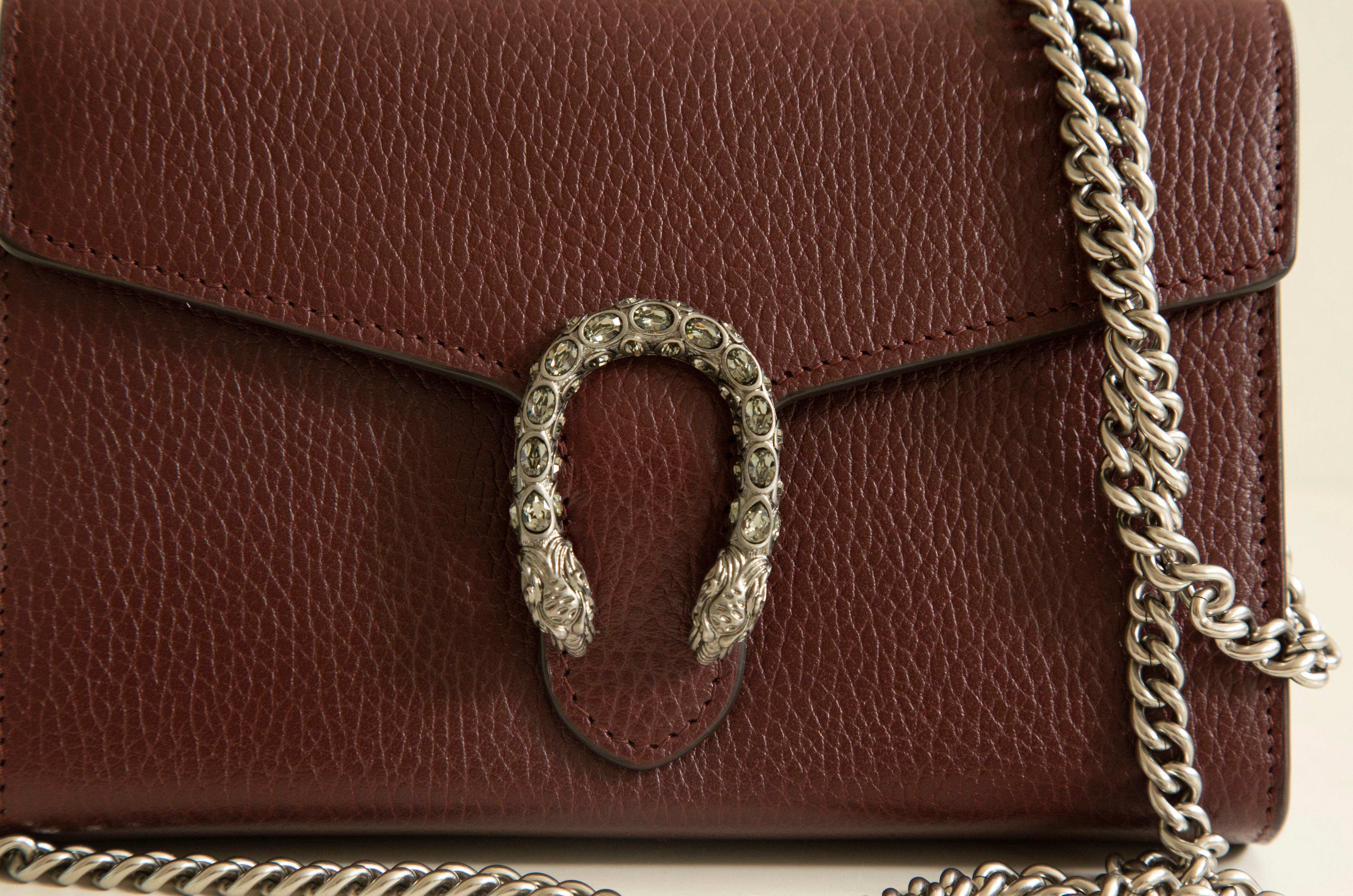 The Gucci Dionysus leather mini chain bag made of burgundy leather with 
old silver toned hardware. The bag features a  tiger head spur closure-a unique detail referencing the Greek god Dionysus, who in myth is said to have crossed the river Tigris