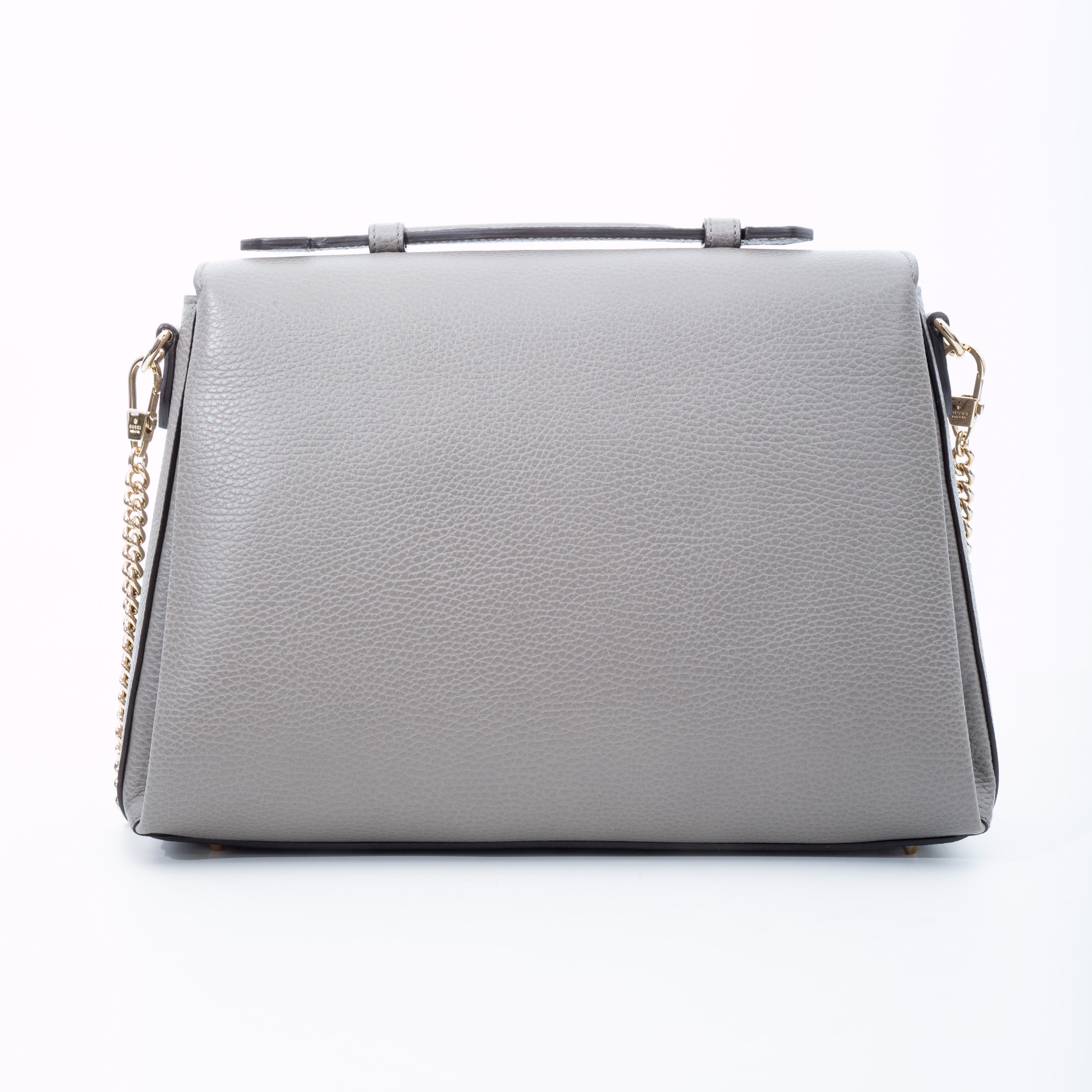This shoulder bag is made of grained calfskin leather in grey. The bag features a waist length flat leather handle & silver chain link shoulder strap, a front flap with a polished gold interlocking GG emblem, protective feet at base and a