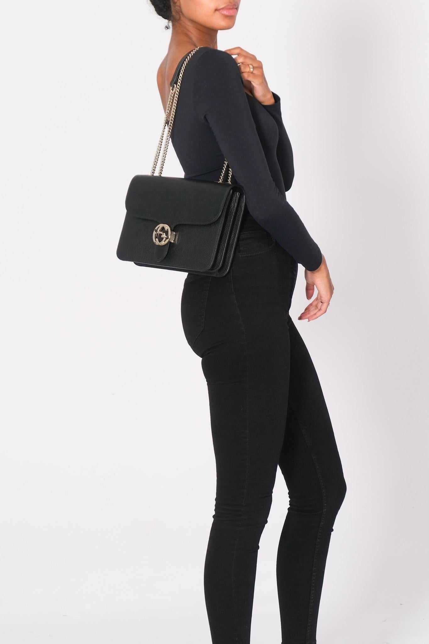 This shoulder bag is made of grained black calfskin leather. The bag features a polished light gold chain link shoulder strap with a leather shoulder pad, and a matching gold interlocking GG flip-lock on the crossover flap. This opens the bag to a