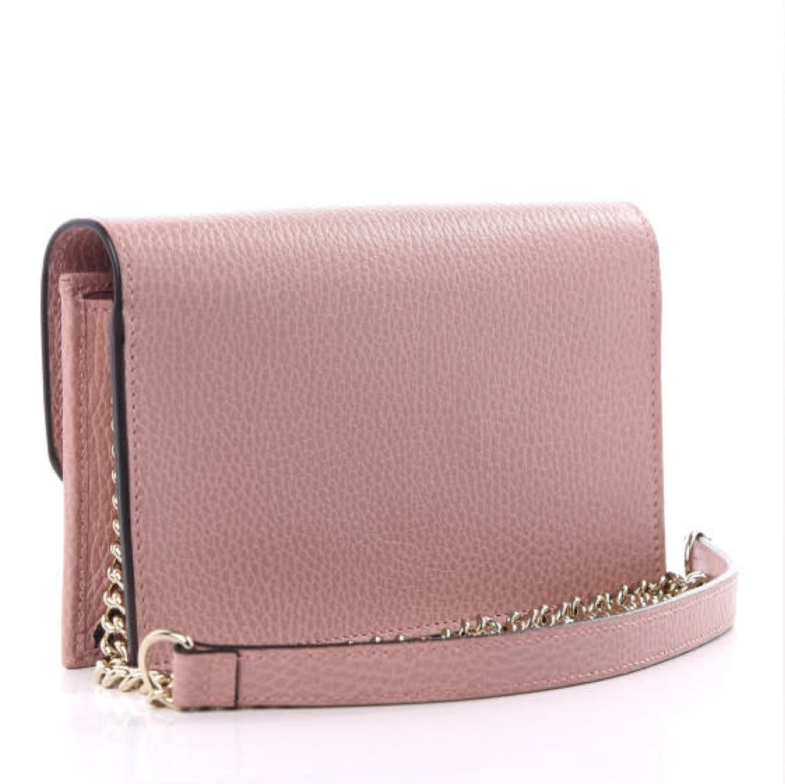 This shoulder bag is made of textured calfskin leather in a dusty pink. This bag features a long aged gold chain shoulder strap and a Gucci GG logo on the front flap. The flap opens to a partitioned leather and black fabric interior with card slot
