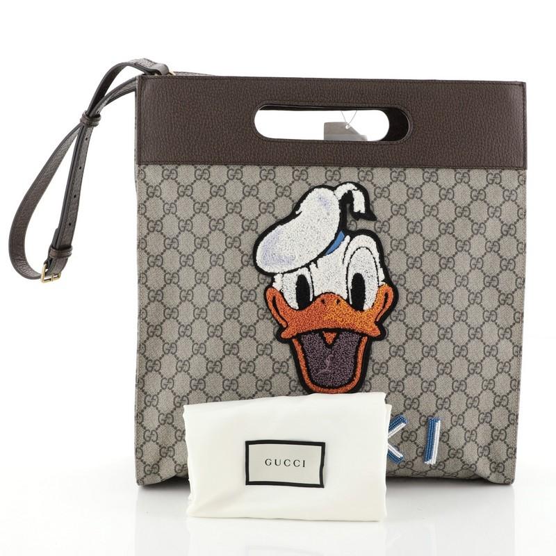 This Gucci Donald Duck Soft Tote Embroidered GG Coated Canvas, crafted from brown embroidered GG coated canvas, features inset handles, adjustable leather shoulder strap, embroidered Donald Duck and Gucci appliqués on the front, embroidered appliqué