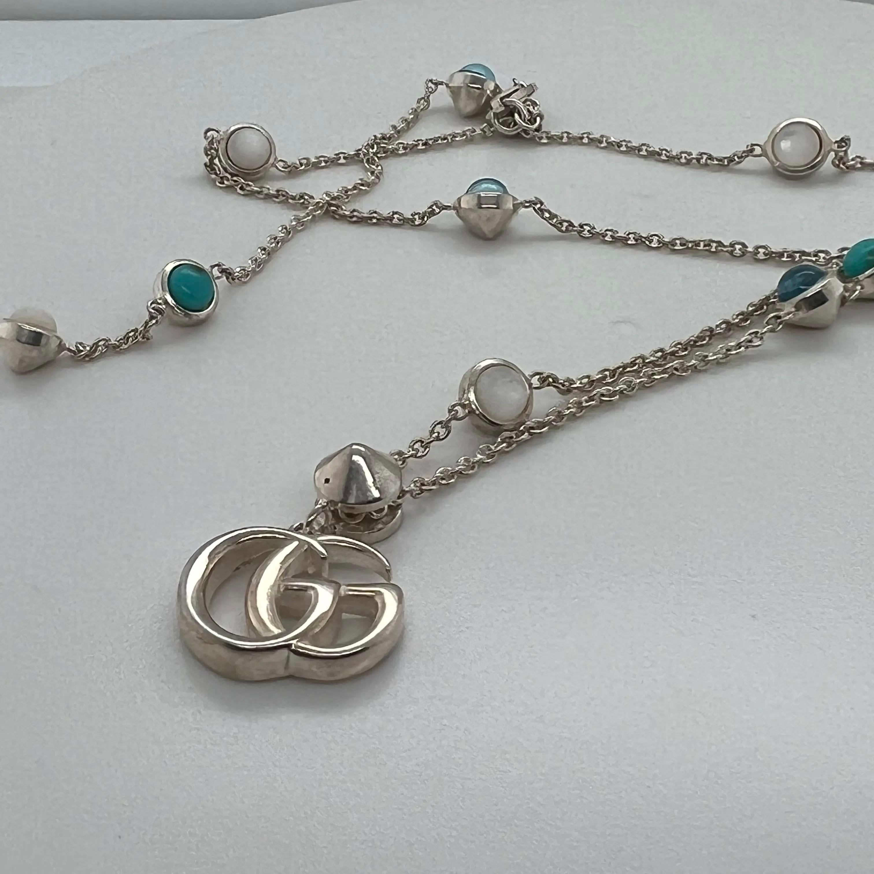 The GUCCI Double G pendant hangs from a 925 sterling silver necklace, enriched with mother of pearl, turquoise colored resin, and topaz stones. Necklace length: 17 inches. Pendant size: 14.4mm x 11.5mm. Secured with a lobster lock. Made in Italy.