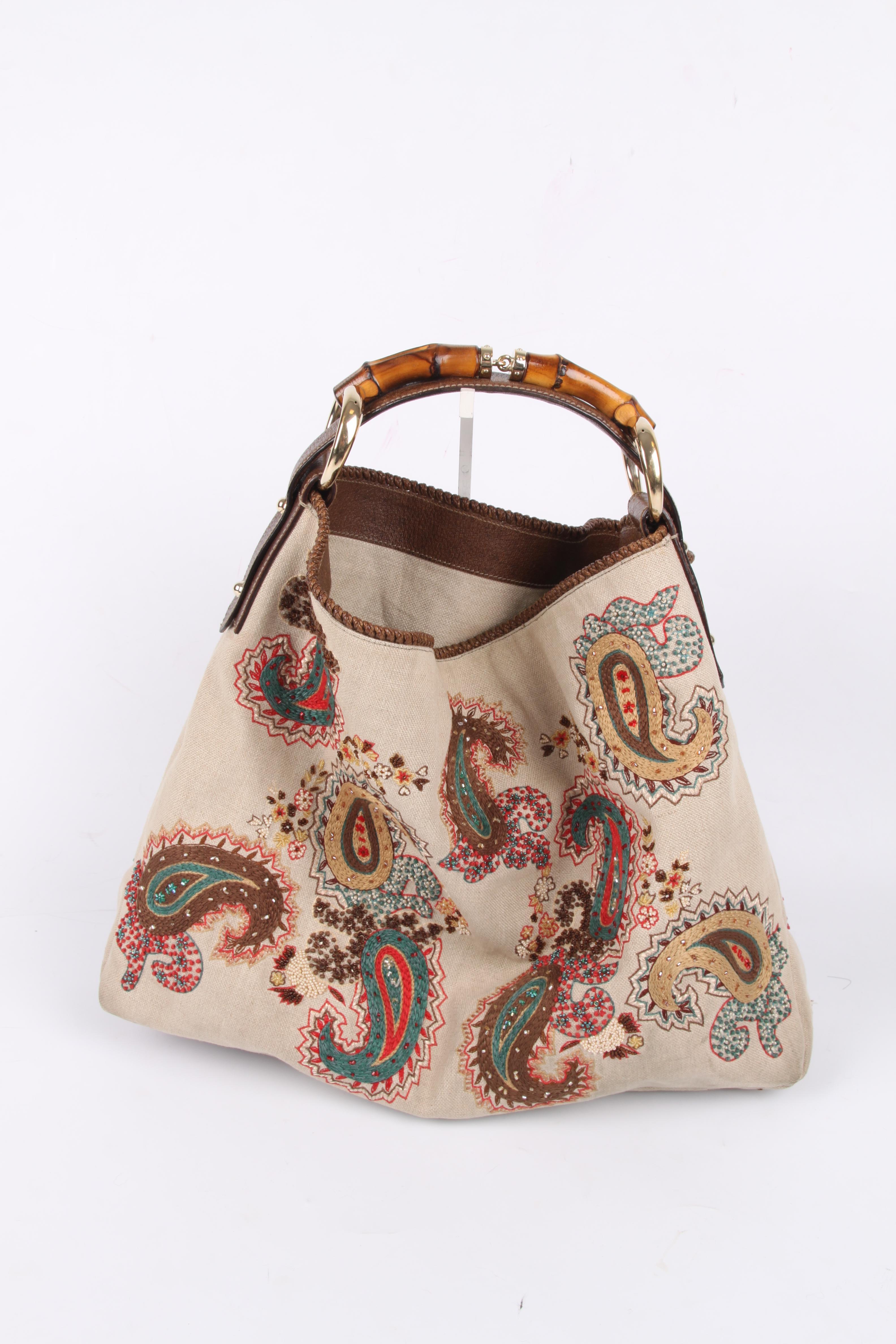Gucci made this large embroidered canvas bag with bamboo handle.

A paisley design in red, beige, taupe and green is embroidered on the bag at the front, back and bottom.

On top some dark brown leather detailing and a bamboo handle with gold-tone