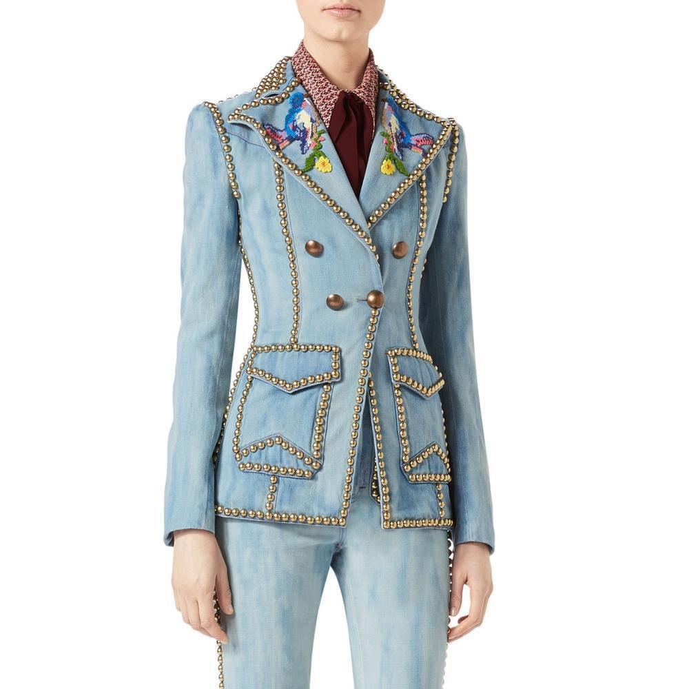 A fitted double-breasted denim jacket gave a new look to the denim collection. Outlined with metal studs with a cross-stitch style embroidery of birds on the lapels.
Gucci blazer jacket in blue stone-washed denim.
Golden metal dome studs outline