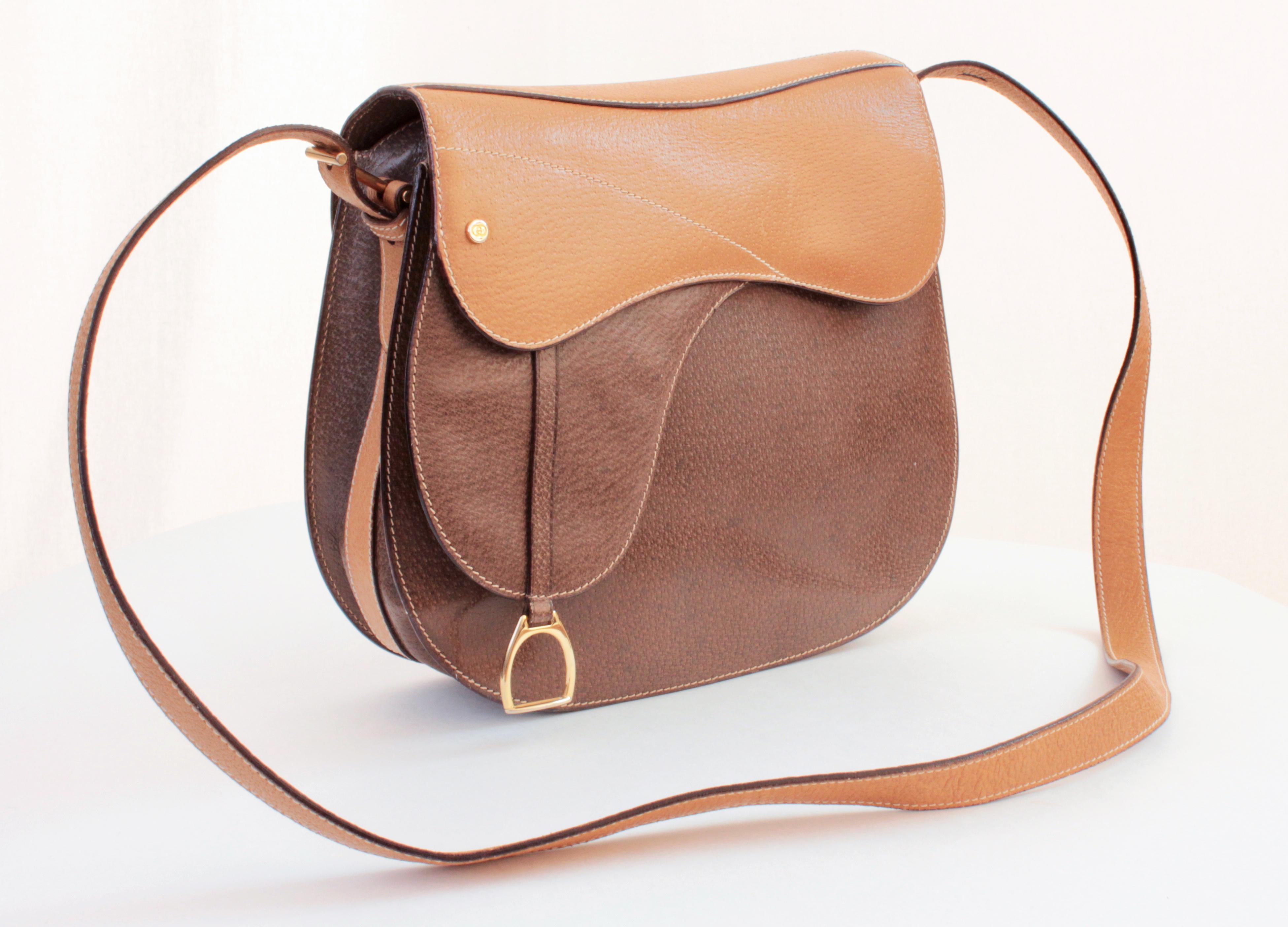 This saddle shaped bag with stirrup charm was made by Gucci, most likely in the early 1980s. Made from pigskin leather in tan and brown, it features an adjustable shoulder strap and inside, there's a flat zip pocket. In excellent condition for its