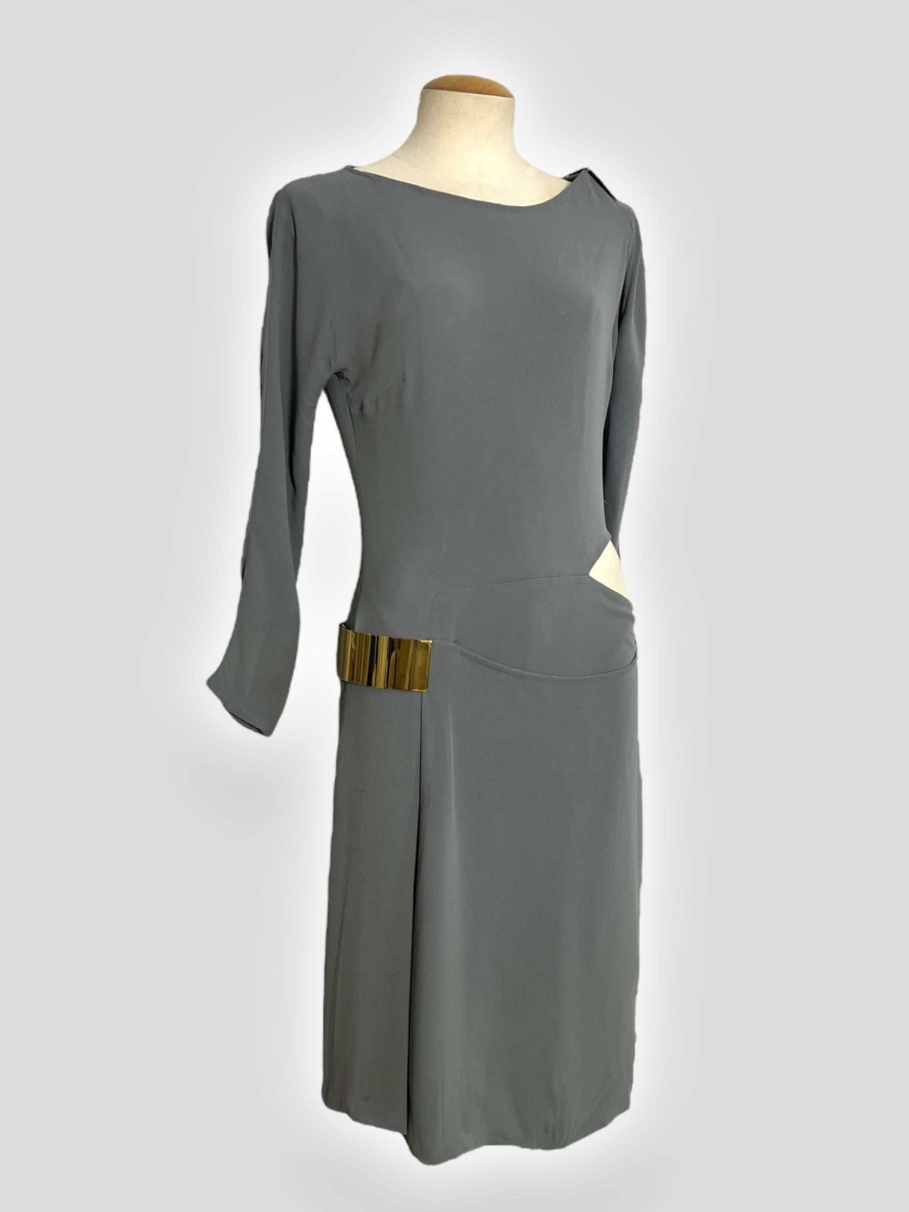A sleek and sophisticated Gucci Fall 2010 runway dress, crafted from luxurious khaki-toned silk. The dress features a modern asymmetrical neckline, structured draping, and a striking cut-out detail at the hip accentuated by a gold-tone metal