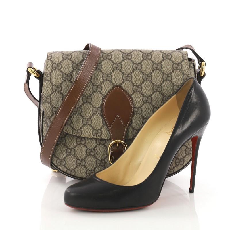 This Gucci Flap Saddle Bag GG Coated Canvas Small, crafted in brown GG coated canvas, features an adjustable shoulder strap and gold-tone hardware. It opens to a brown microfiber with zip pocket. **Note: Shoe photographed is used as a sizing
