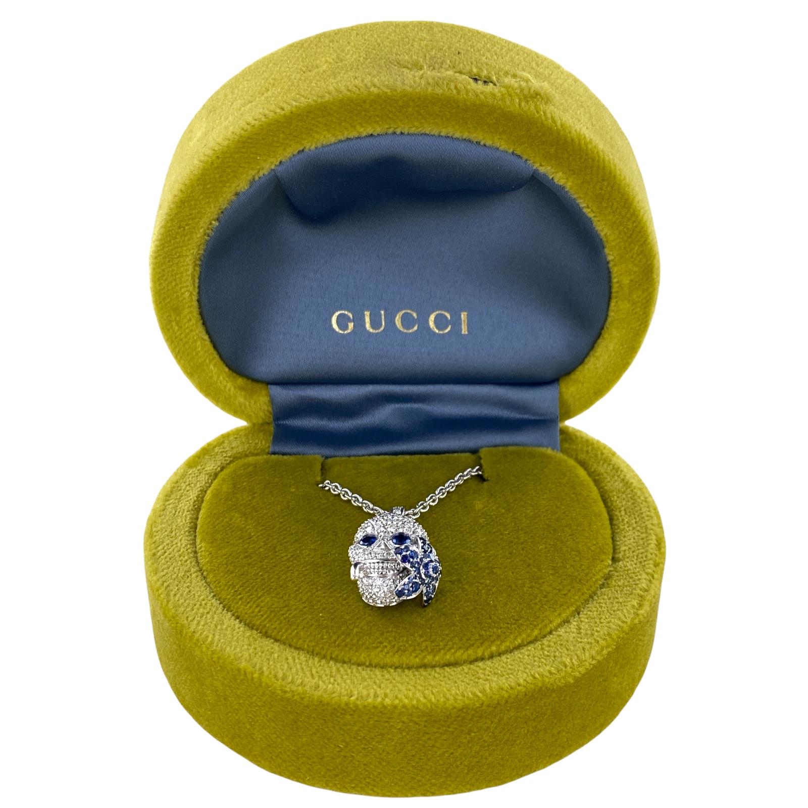 Gucci diamond blue sappphire skull pendant necklace fashioned in 18 karat white gold. The pendant features round brilliant cut diamonds, natural blue sapphires, and measures 1.0 x .50 inches. The pendant is on the original Gucci chain that can be