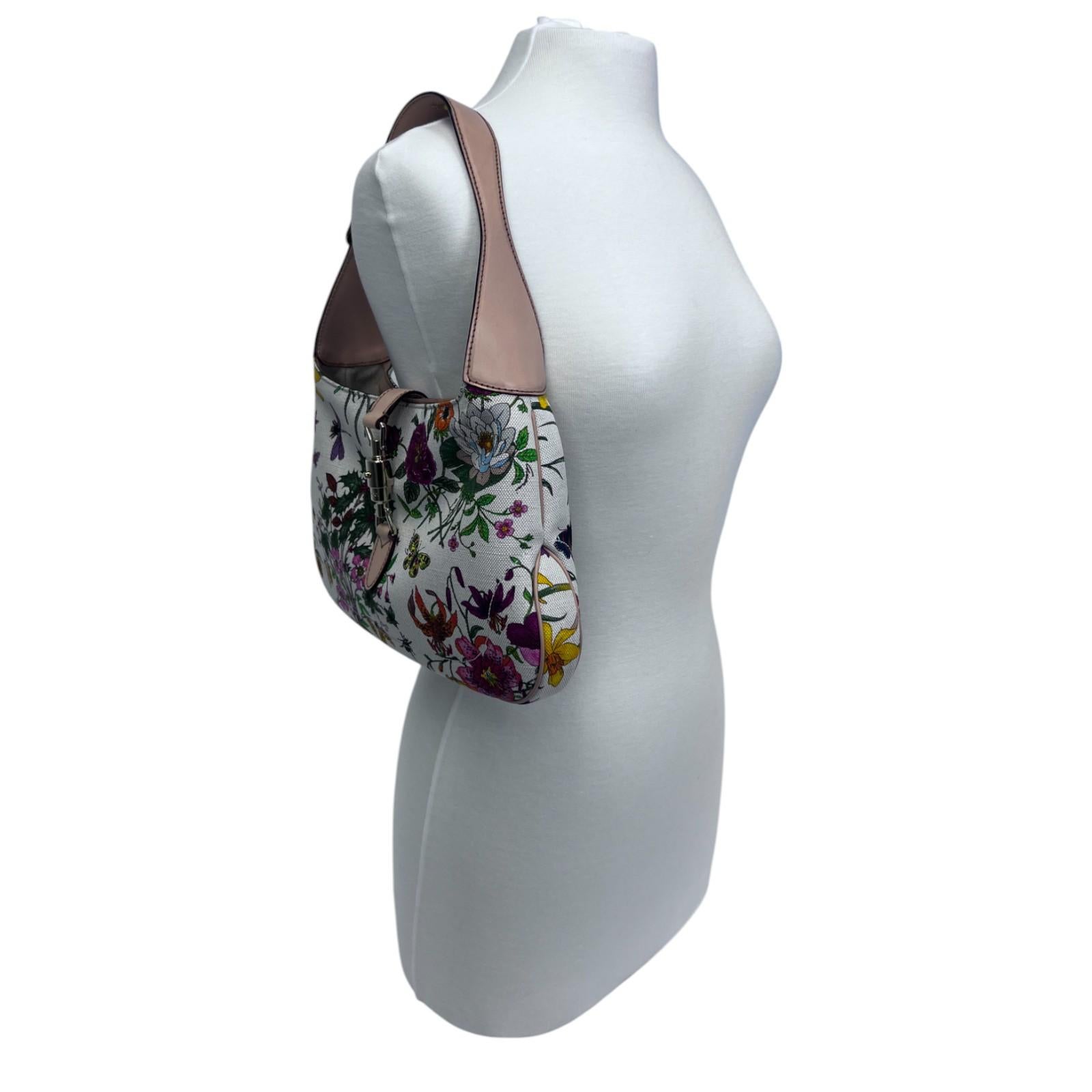 Die Jackie O Hobo Bag von Gucci ist eine zeitlose Ikone, die mit einem romantischen Touch neu interpretiert wurde. Sie zeigt das ikonische Flora-Motiv des Hauses auf neutralem Canvas, akzentuiert mit goldfarbener Hardware und Glattlederbesätzen.