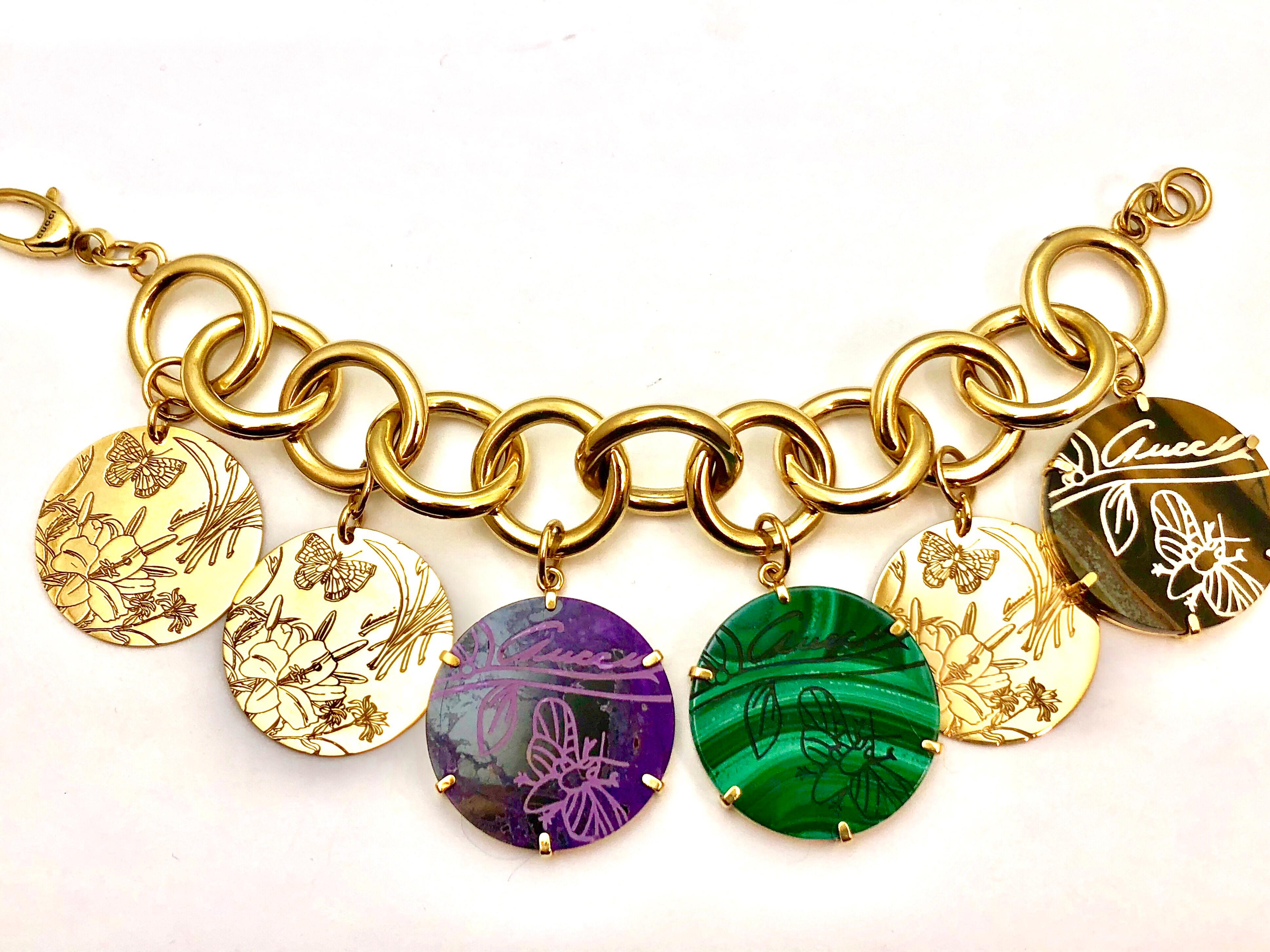 A Gucci Flora St. Tropez 18 karat yellow gold bracelet with Malachite, Sugilite, Tiger's Eye, and gold etched charms.  The bracelet is designed with circular links, and has a total of six discs hanging from the links with etchings of butterflies and