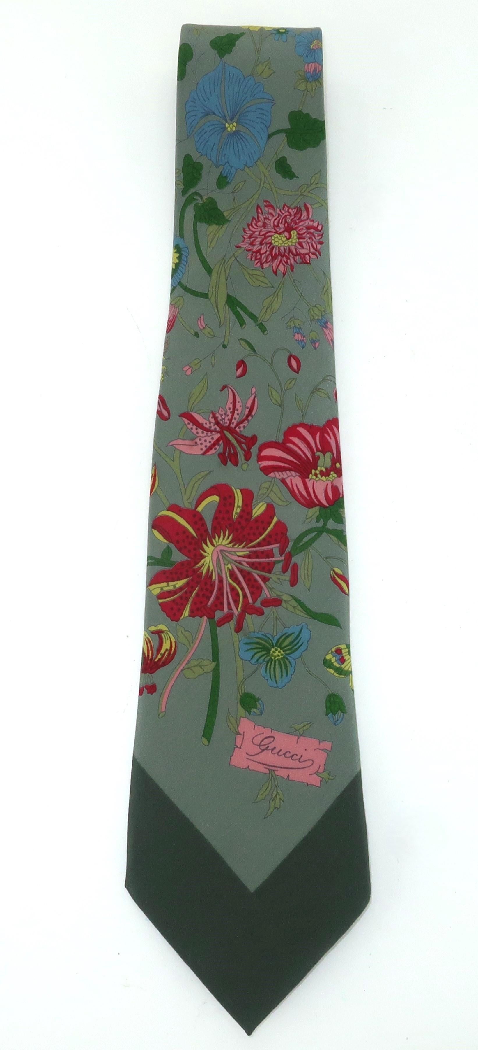 Magnifique cravate en soie florale Gucci dans les tons gris tourterelle, rouge, vert, jaune, bleu et rose.  Le nom Gucci apparaît dans l'imprimé et dans l'imprimé jacquard de la doublure.  Conçue pour les hommes mais tout aussi merveilleuse pour