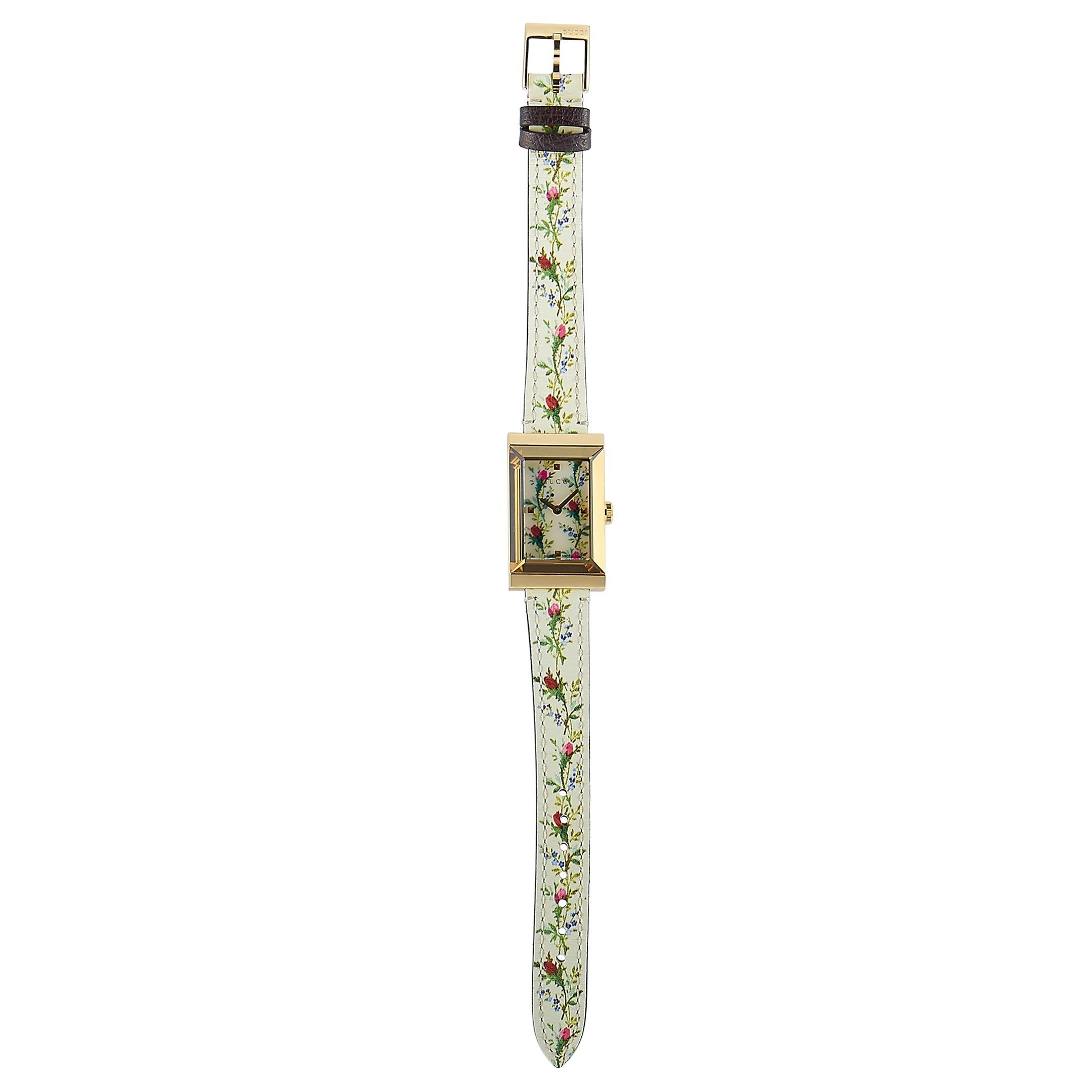The Gucci G-Frame watch, reference number YA147407, is presented with a yellow gold PVD-plated stainless steel case that is water-resistant to 30 meters. The case is mounted onto a leather strap with floral motifs, secured on the wrist with a tang