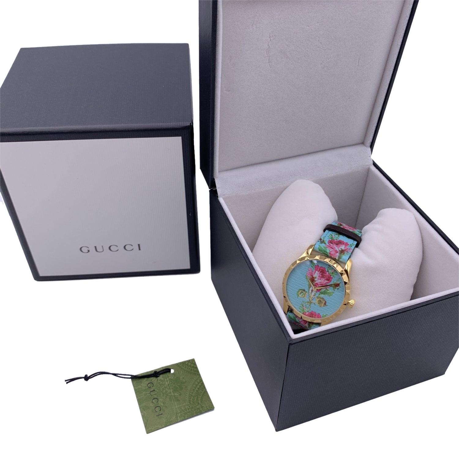 Gucci 'G-Timeless' gold metal stainless steel watch, Model 126.4. Round gold metal case (40 mm - crown included) with floral print leather strap. Aqua floral printed dial with gold metal GUCCI signature on the face. Two hands. Sapphire crystal.