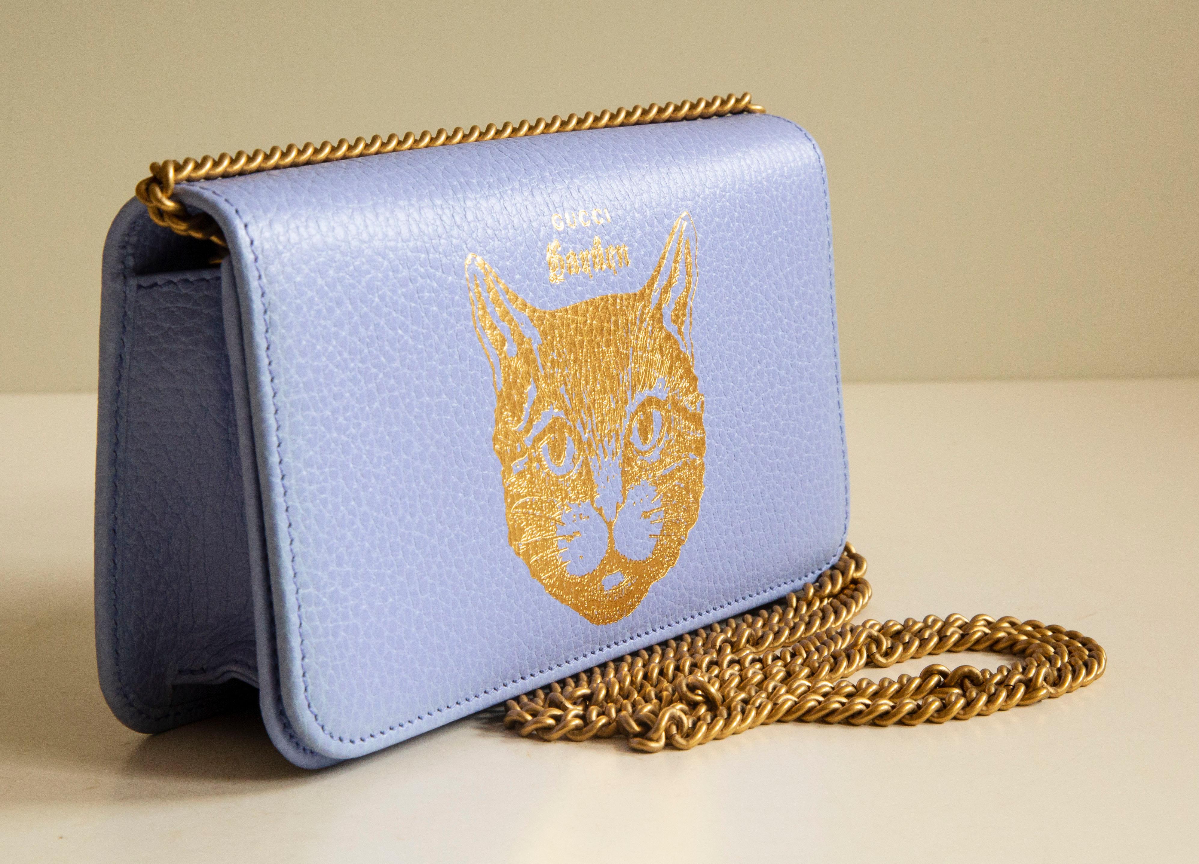A Gucci Garden calfskin limited edition cat chain pouch in light Lila color. The bag opens and closes with a magnetic flap and there is one key hanger on the side of the bag. The interior is made of blue fabric. The condition is excellent without