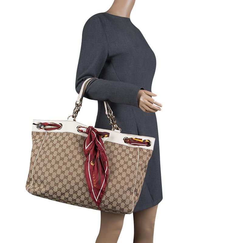 Take your style a notch higher with this Positano tote from Gucci. Cut out of GG canvas, the bag features two handles, a spacious fabric interior and a scarf laced around the top. The tote is complete with gold-tone hardware and it is truly a
