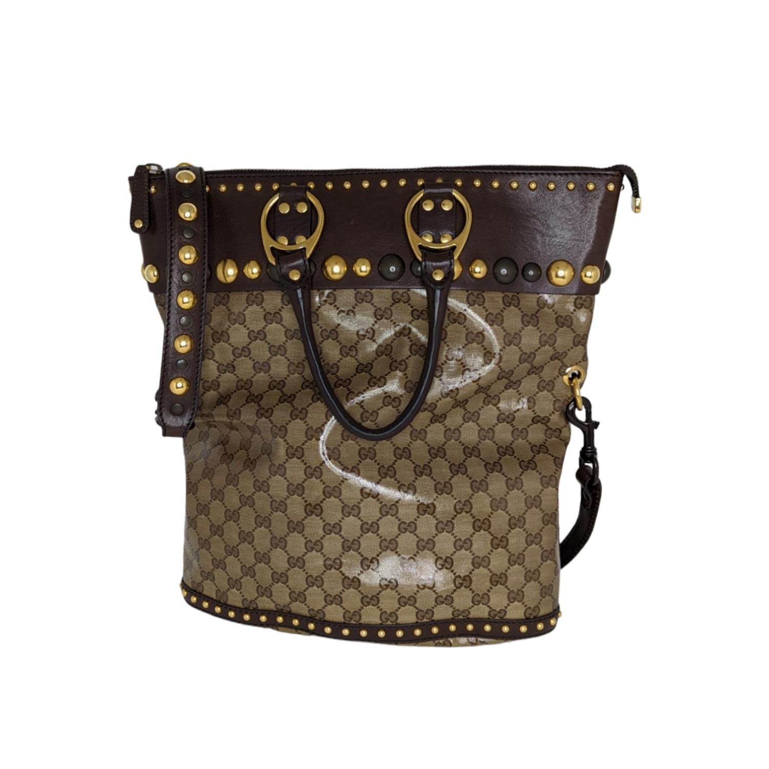 Make a bold statement with this top handle handbag from Gucci's Babouska collection. Crafted from coated GG monogram canvas with brown leather trim, the exterior is accented with large round studs and dual rolled handles. Its plaid fabric lined