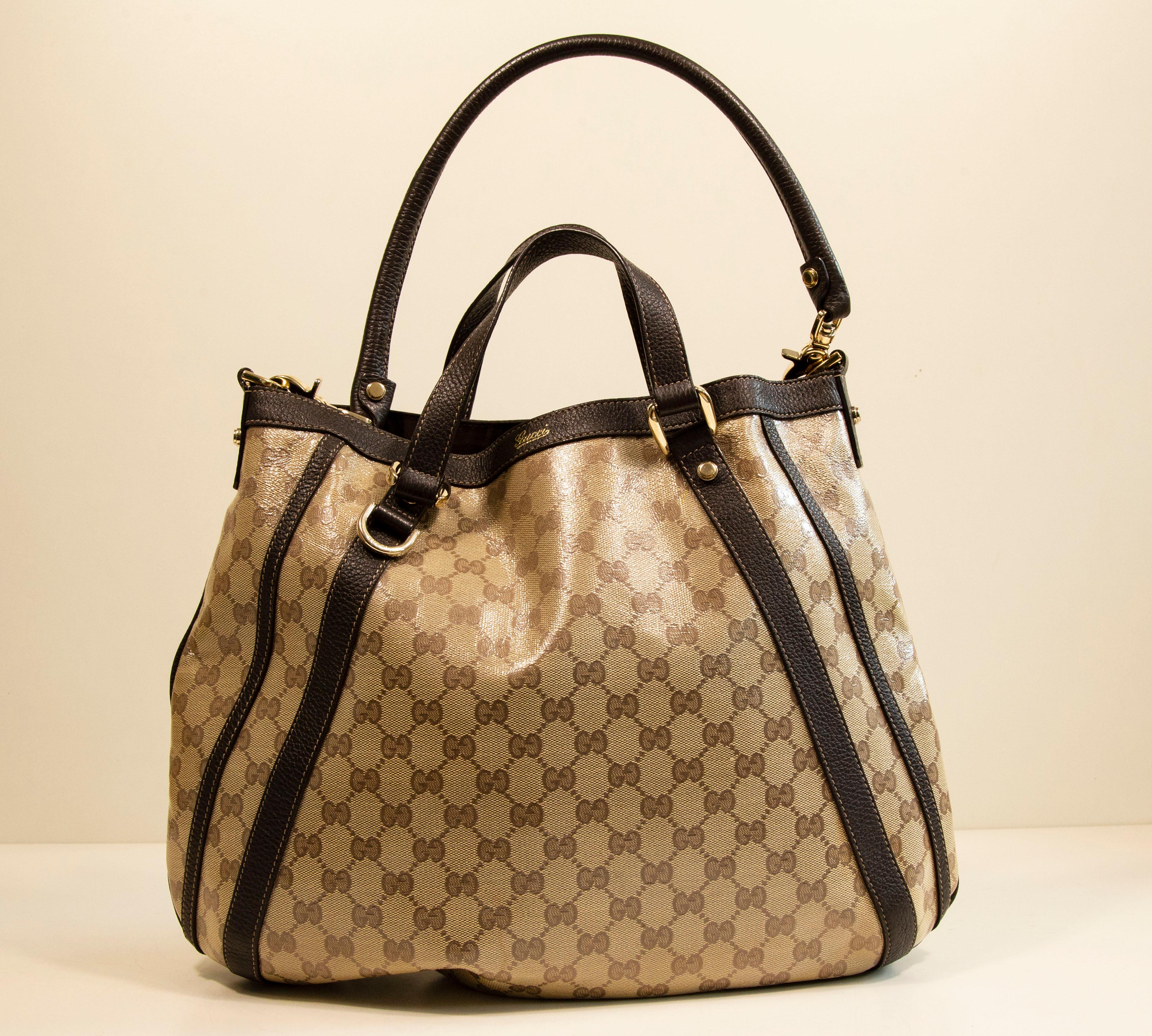 Gucci GG Crystal Canvas Abbey D Ring Convertible Tote / Umhängetasche / 2-Wege-Tasche. Die Tasche ist aus vinylbeschichtetem Segeltuch mit dem GG-Web und braunem Lederbesatz gefertigt. Die Beschläge sind in hellem Goldton gehalten. Das Innere ist