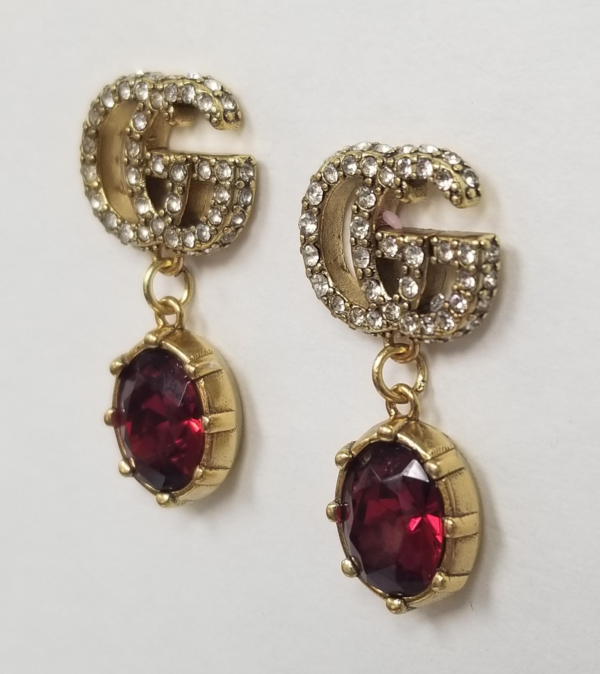  A red faceted crystal Earrings combines with the crystal Double G detail, forming a sparkling Earrings that completes these earrings in aged gold-toned metal.

    Metal with aged gold finish
    Crystal encrusted Double G detail
    Red crystal