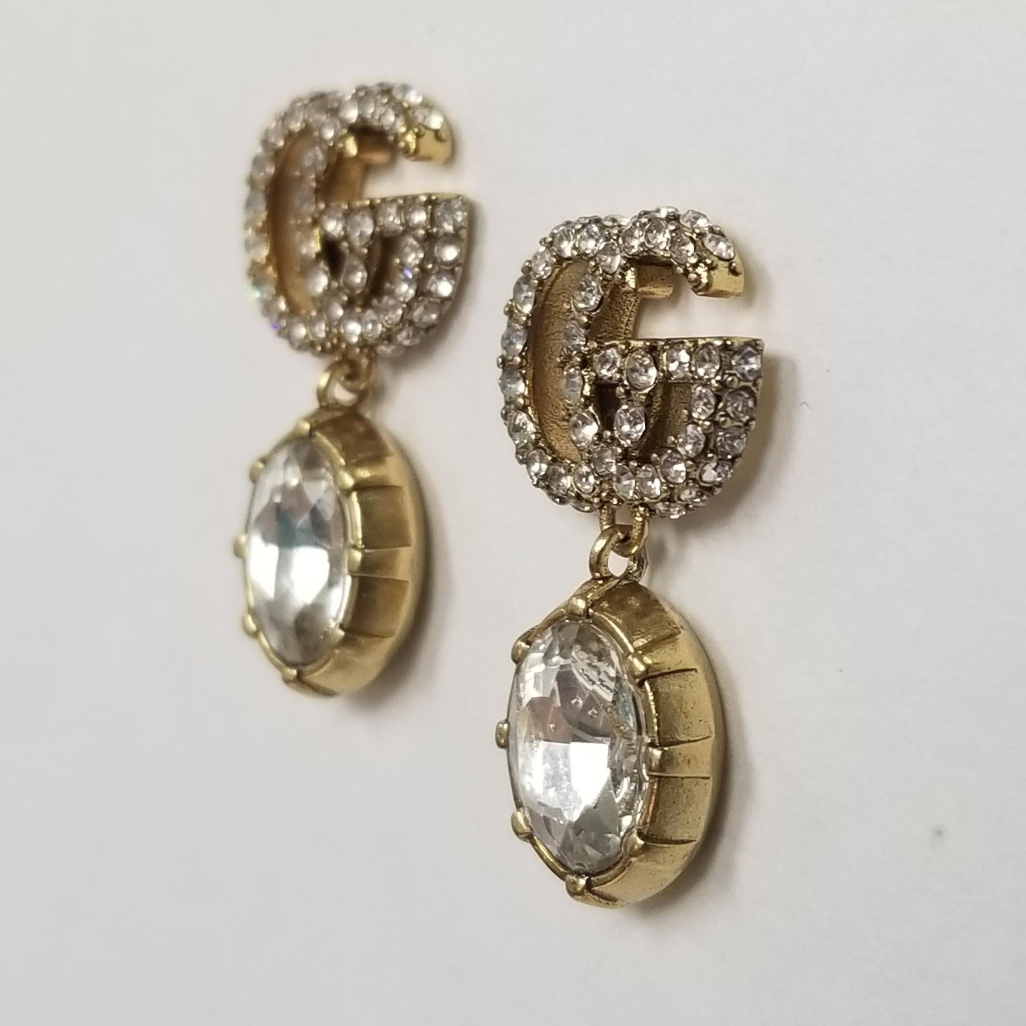  A white faceted crystal Earrings combines with the crystal Double G detail, forming a sparkling pendant that completes these earrings in aged gold-toned metal.

    Metal with aged gold finish
    Crystal encrusted Double G detail
    White crystal
