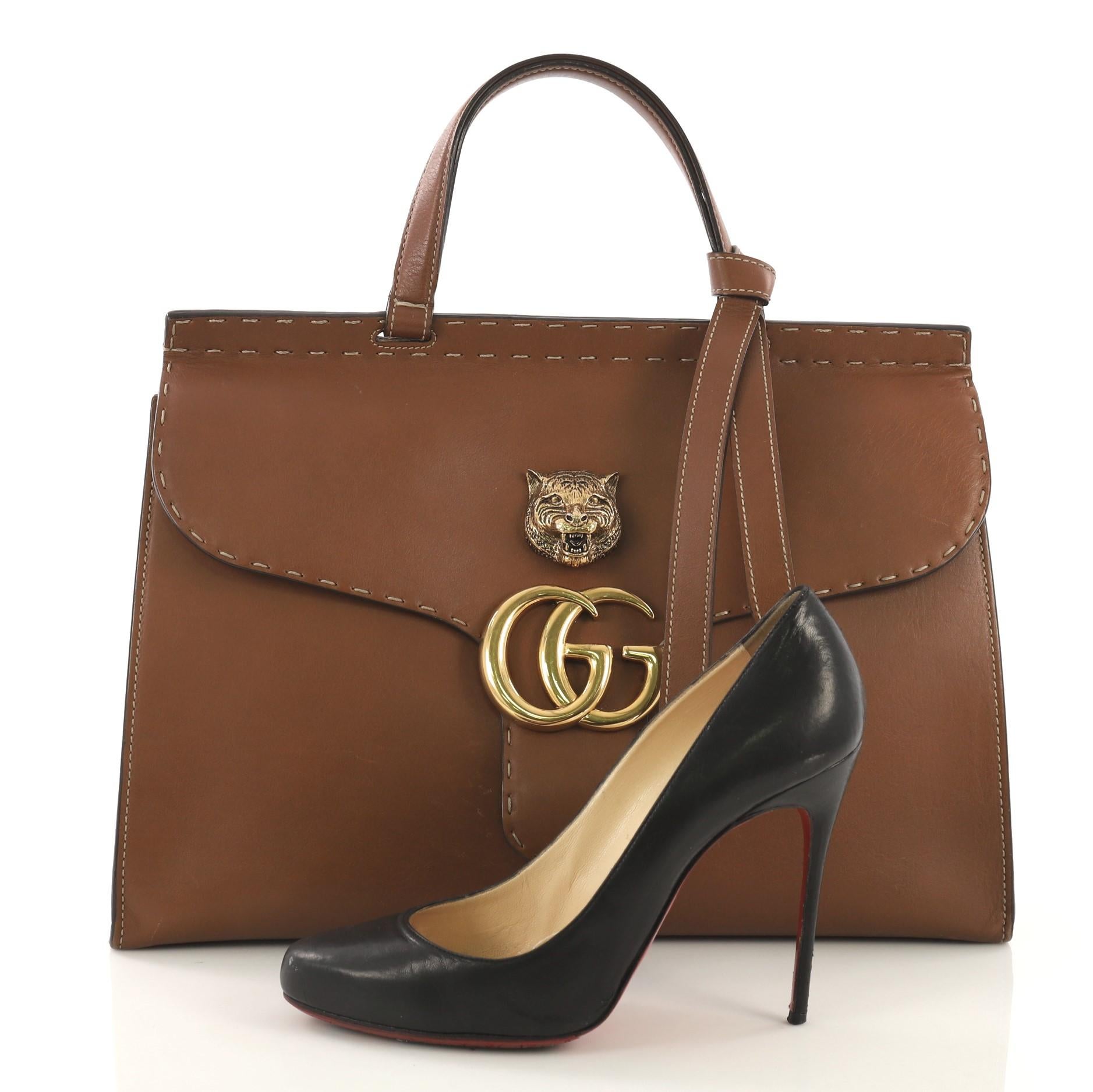 This Gucci GG Marmont Animalier Top Handle Bag Leather Medium, crafted in brown leather, features leather top handle, front flap with animalier detail, interlocking GG logo, oversized stitched design, and aged gold-tone hardware. Its snap button