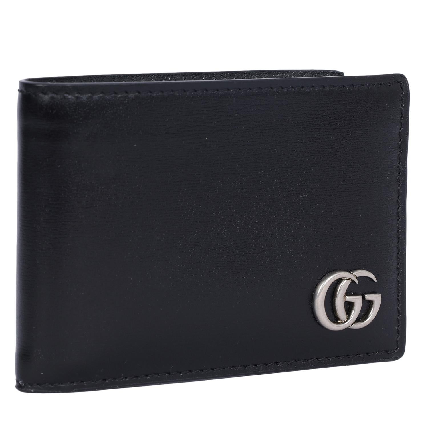 Authentique portefeuille bi-fold GG Marmont de Gucci en cuir noir. 

Un portefeuille fin en cuir noir lisse. Un double G en palladium qui ajoute une touche subtile de logo au portefeuille. Il y a 4 fentes pour cartes et un compartiment pour les