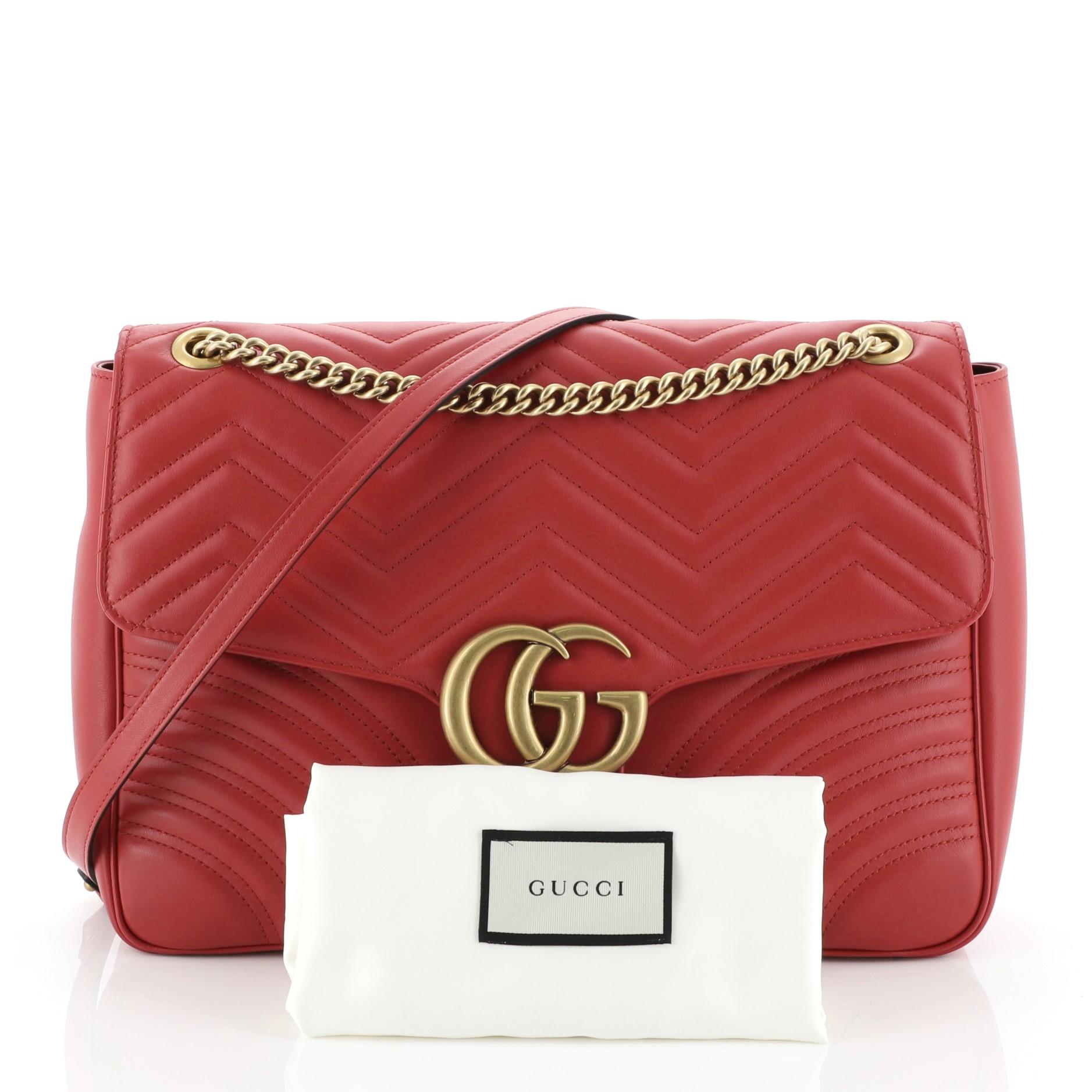 This Gucci GG Marmont Flap Bag Matelasse Leather Large, crafted from red matelasse leather, features a chain-link shoulder strap with leather pad, flap top with GG logo, and aged gold-tone hardware. Its push-lock closure opens to a neutral