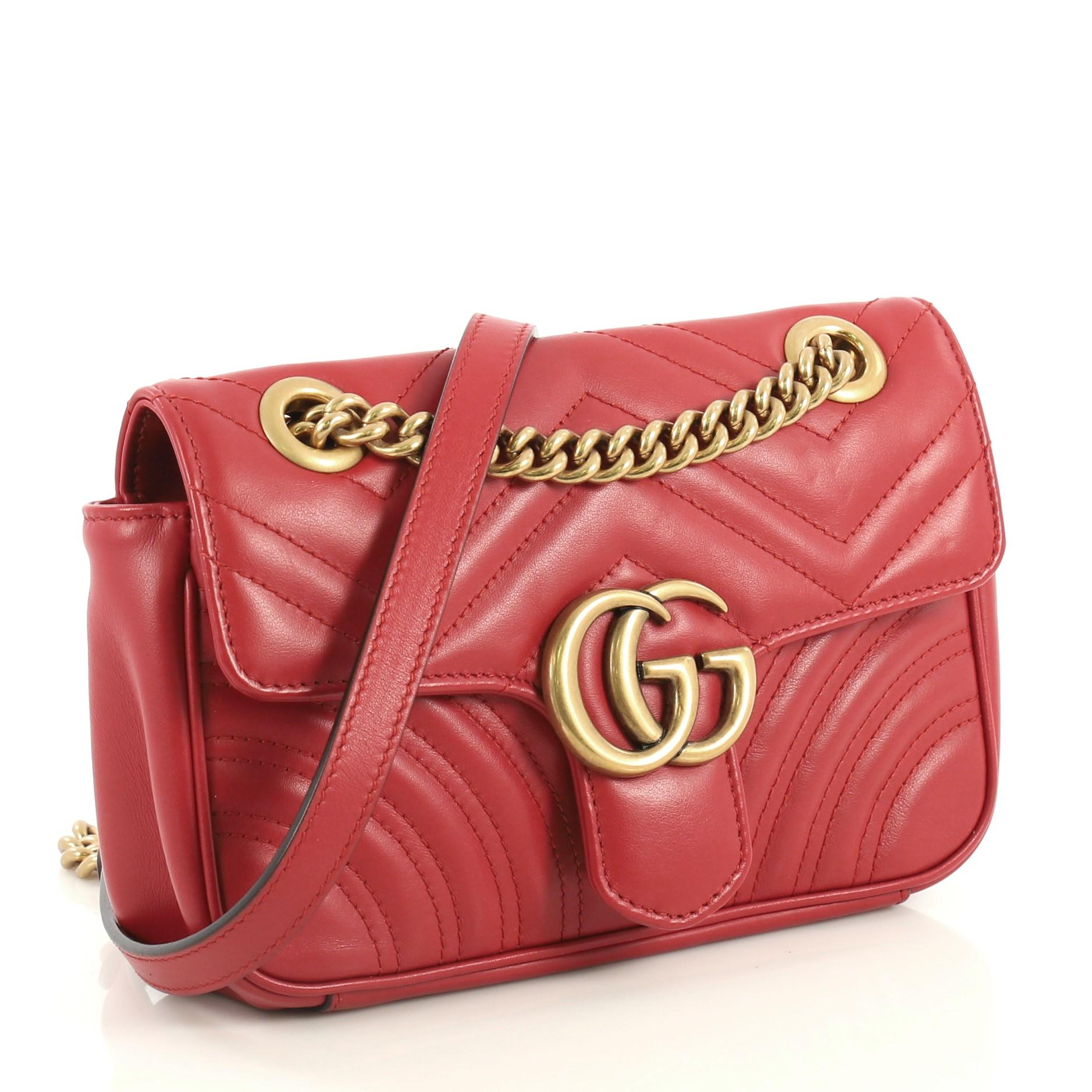 This Gucci GG Marmont Flap Bag Matelasse Leather Mini, crafted from red matelasse leather, features a chain link strap with leather pad, flap top with GG logo, and aged gold-tone hardware. Its push-lock closure opens to a neutral microfiber interior