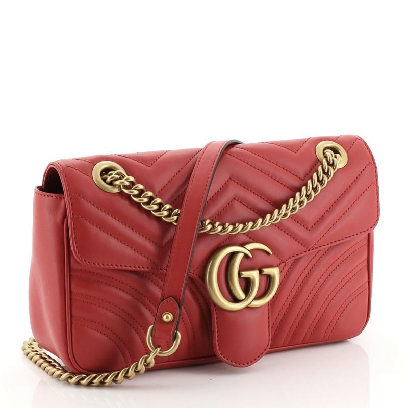 This Gucci GG Marmont Flap Bag Matelasse Leather Small, crafted from red matelasse leather, features chain link strap with leather pad, flap top with GG logo, and aged gold-tone hardware. Its push-lock closure opens to a neutral microfiber interior