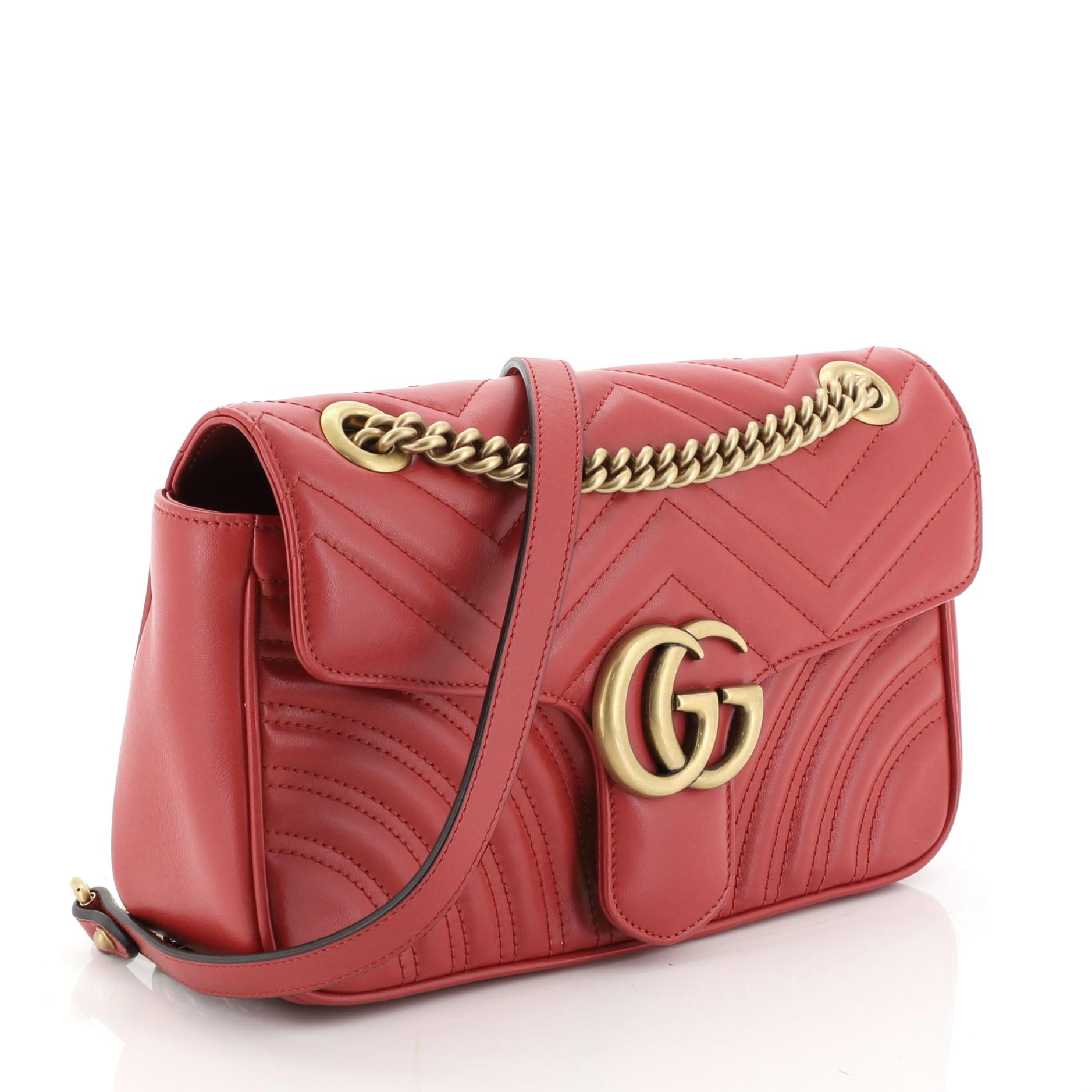 This Gucci GG Marmont Flap Bag Matelasse Leather Small, crafted from red matelasse leather, features a chain link strap with leather pad, flap top with GG logo, and aged gold-tone hardware. Its push-lock closure opens to a neutral microfiber