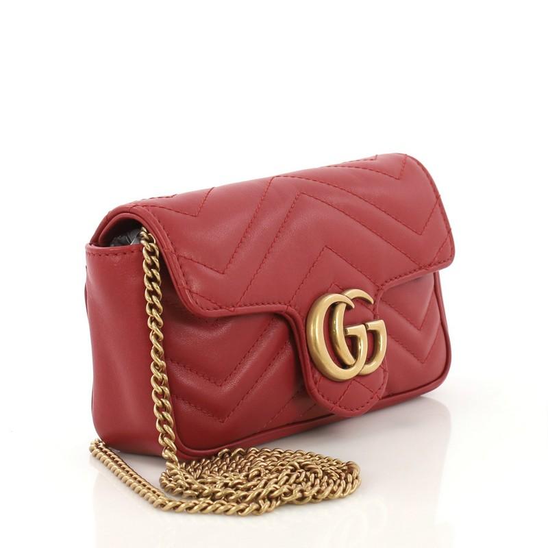 This Gucci GG Marmont Flap Bag Matelasse Leather Super Mini, crafted from red matelasse leather, features a chain link strap with leather pad, flap top with GG logo, and aged gold-tone hardware. Its push-lock closure opens to a nude microfiber