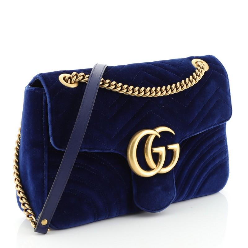 This Gucci GG Marmont Flap Bag Matelasse Velvet Medium, crafted from blue matelasse velvet, features chain link strap with leather pad, flap top with GG logo, and aged gold-tone hardware. Its push-lock closure opens to a pink satin interior with zip