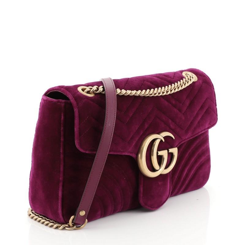 This Gucci GG Marmont Flap Bag Matelasse Velvet Medium, crafted from purple matelasse velvet, features chain link strap with leather pad, flap top with GG logo, and aged gold-tone hardware. Its push-lock closure opens to a pink satin interior with