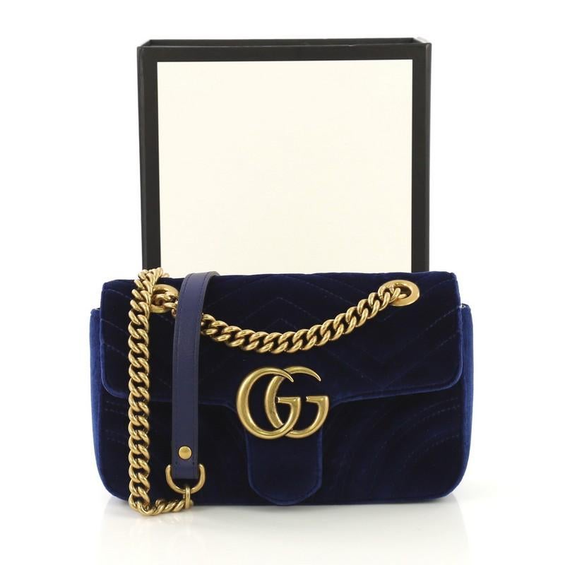 This Gucci GG Marmont Flap Bag Matelasse Velvet Mini, crafted from blue matelasse velvet, features chain link strap with leather pad, flap top with GG logo, and aged gold-tone hardware. Its push-lock closure opens to a pink satin interior with slip