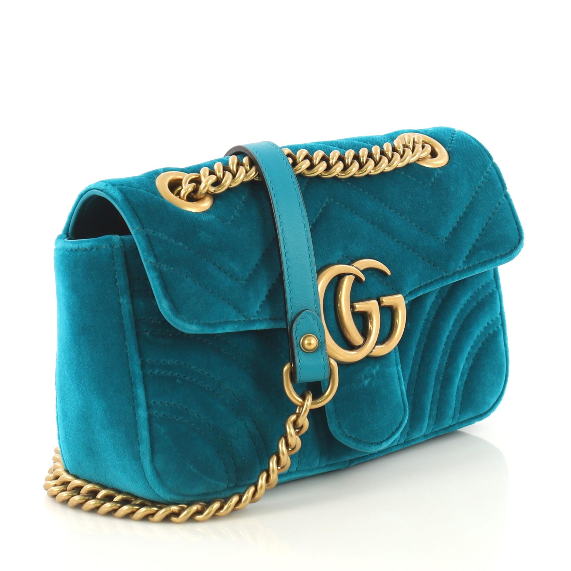 This Gucci GG Marmont Flap Bag Matelasse Velvet Mini, crafted from teal matelasse velvet, features chain link strap with leather pad, flap top with GG logo, and aged gold-tone hardware. Its push-lock closure opens to a pink satin interior with slip