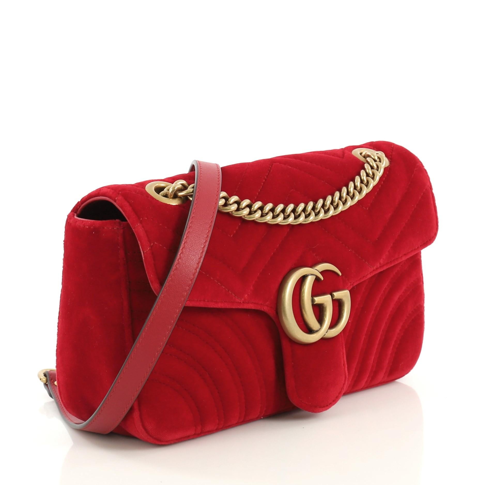 This Gucci GG Marmont Flap Bag Matelasse Velvet Small, crafted from red matelasse velvet, features chain link strap with leather pad, flap top with GG logo, and aged gold-tone hardware. Its push-lock closure opens to a blue satin interior with zip