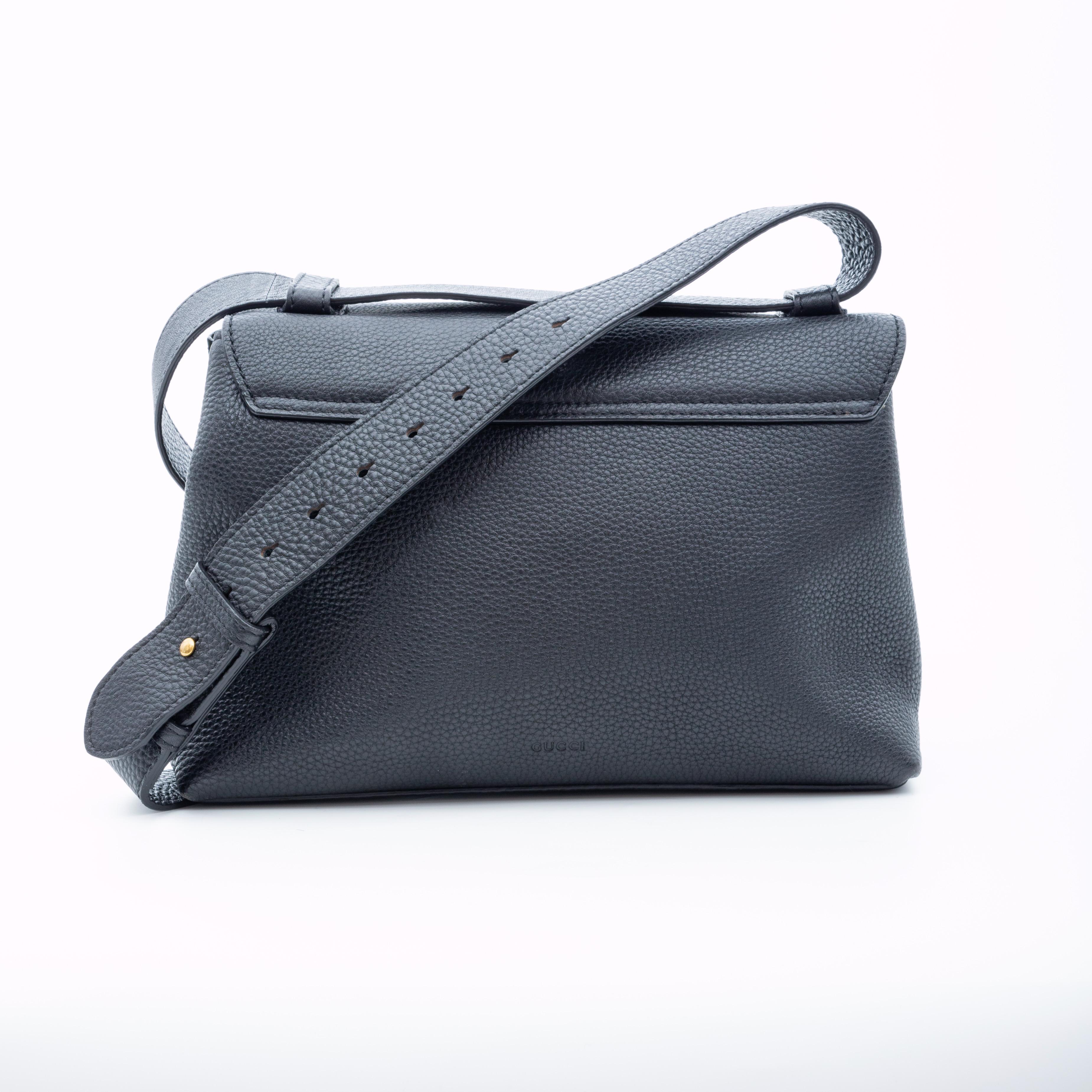 This bag is made with durable grained calfskin in black. The bag features an aged gold tone GG on the front flap, an extra wide flat leather shoulder strap, push lock closure, beige woven fabric lining and a partitioned interior with slip and zip