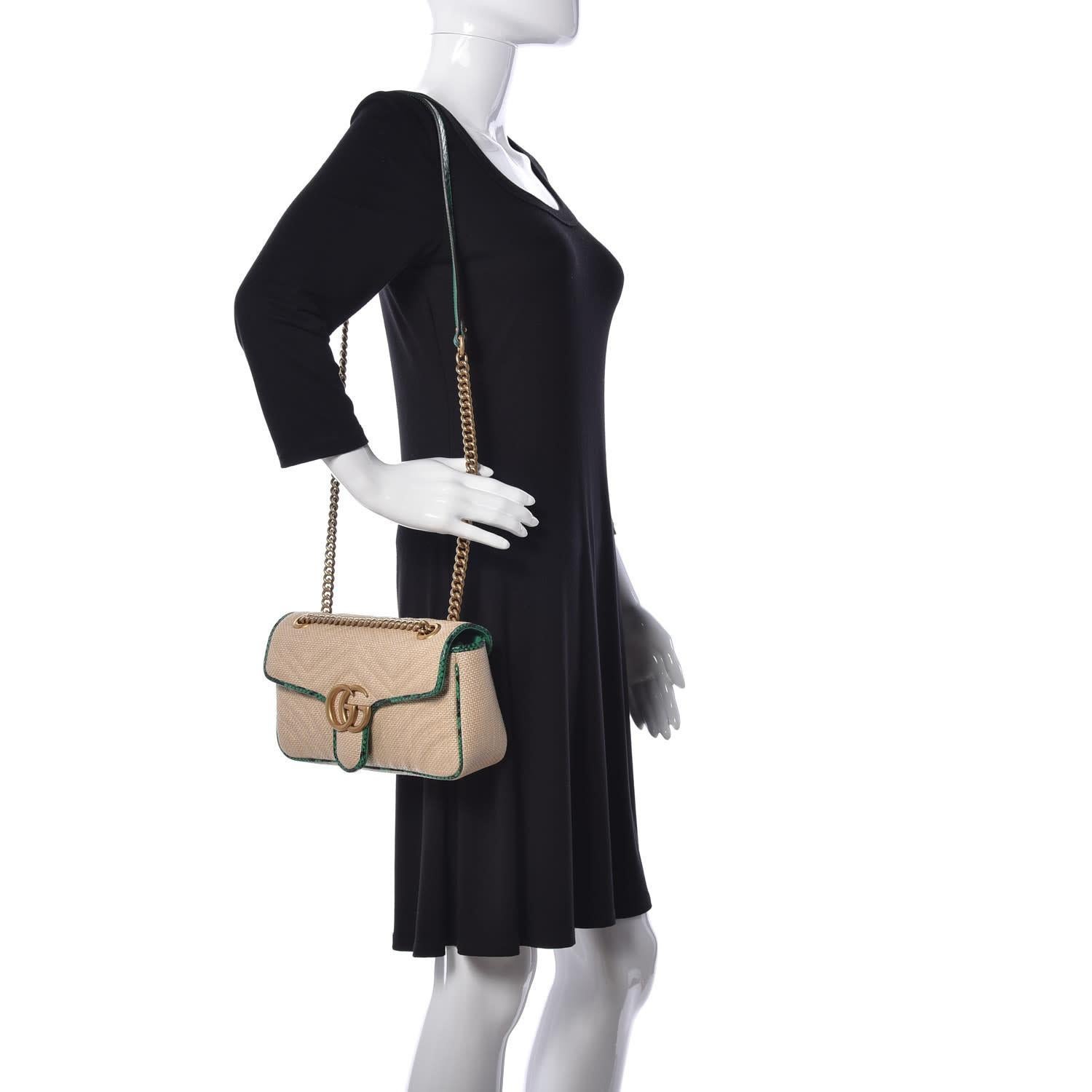 This Gucci shoulder bag is constructed of neutral-toned raffia canvas with a chevron matelassé stitch and finished with green and black snakeskin trim. It features a polished gold chain-link shoulder strap with a leather shoulder pad and the GG