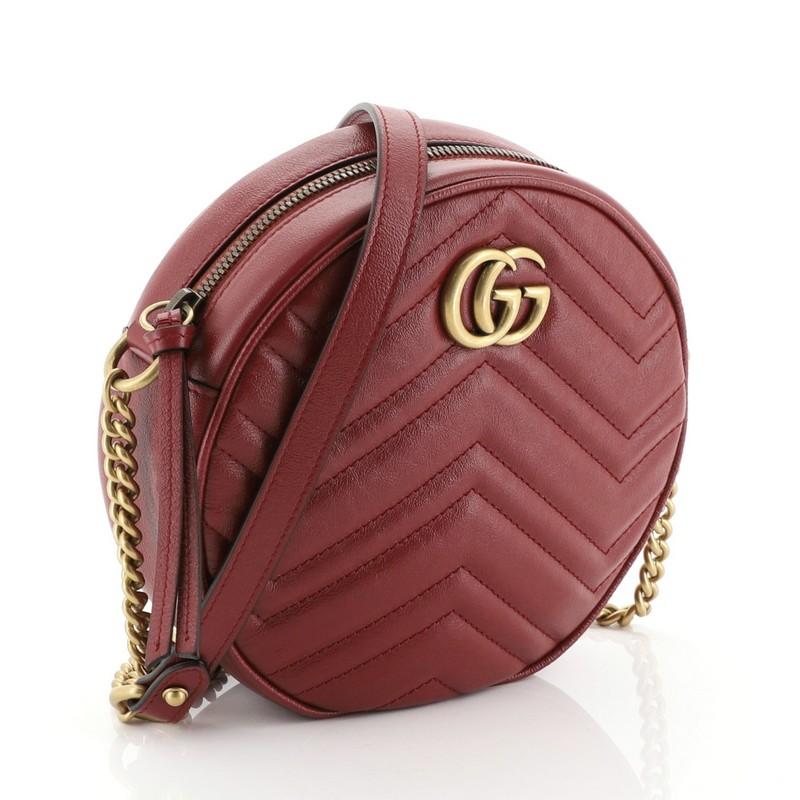 This Gucci GG Marmont Round Shoulder Bag Matelasse Leather Mini, crafted from red matelasse leather, features chain link strap with leather pad, GG logo at the front, and aged gold-tone hardware. Its zip closure opens to a neutral microfiber